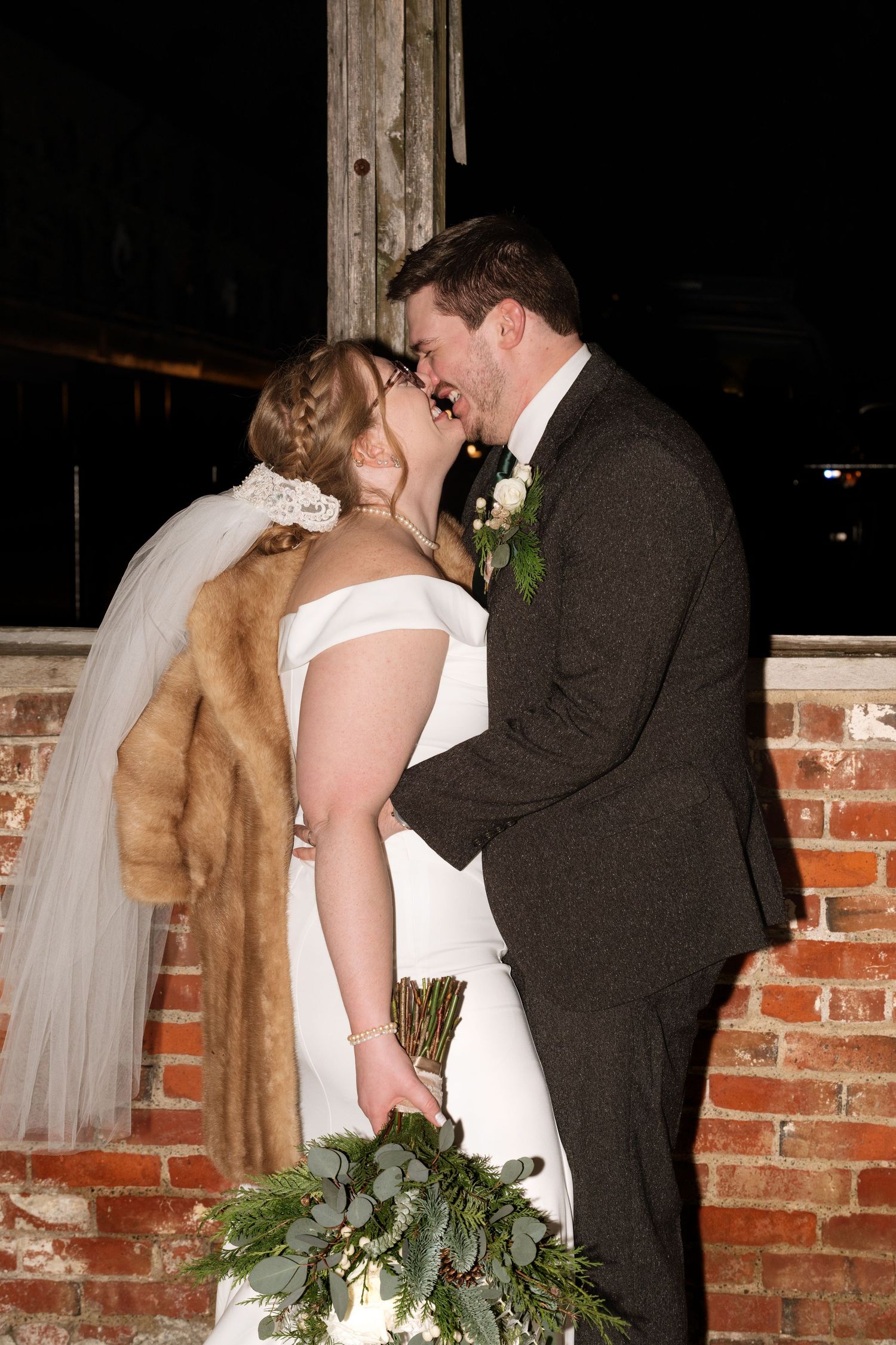 Romantic wedding moment against brick wall with bride wearing fur wrap.