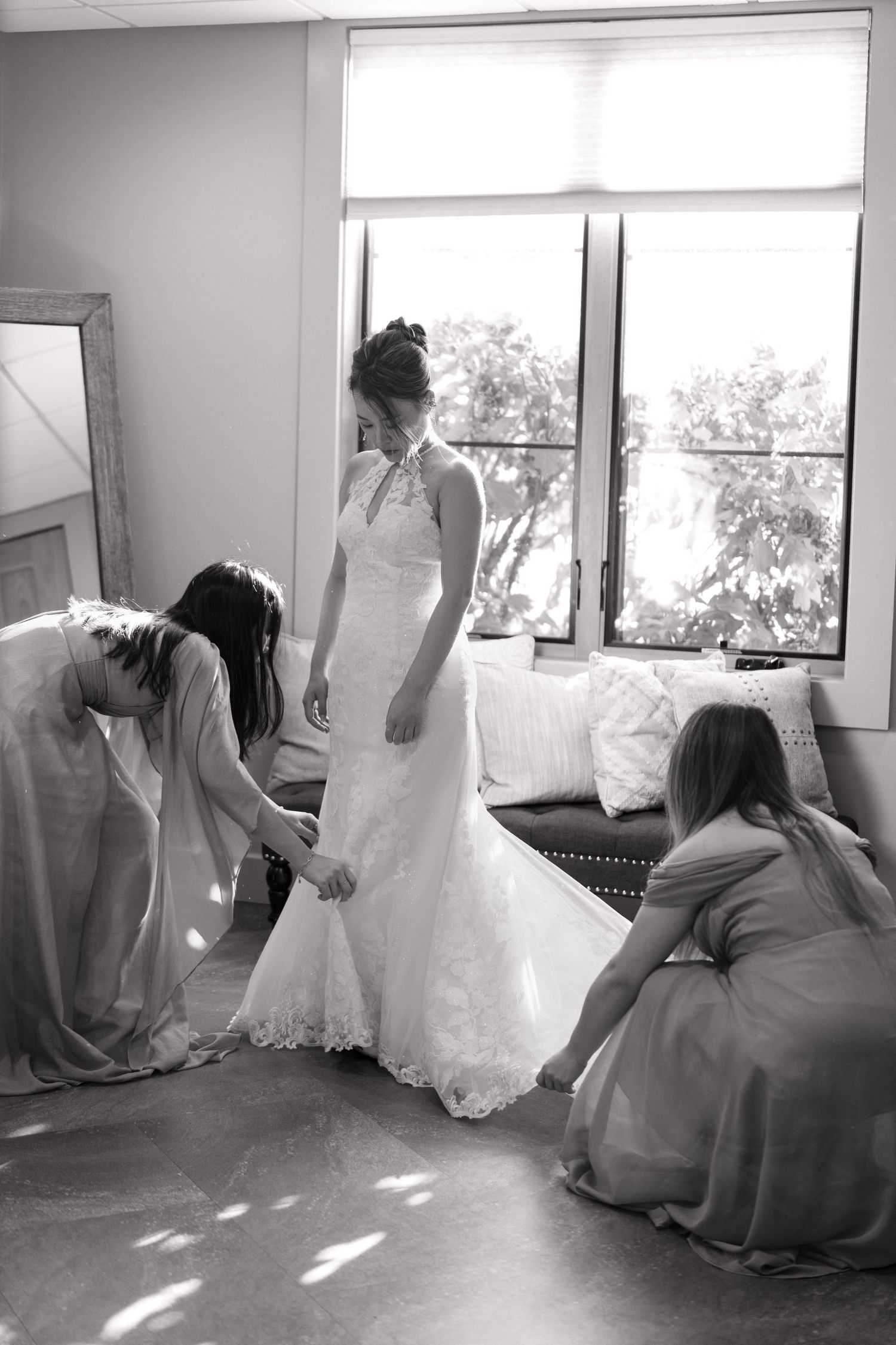 Wedding dress preparation scene in sunlit room with flowing white gown.