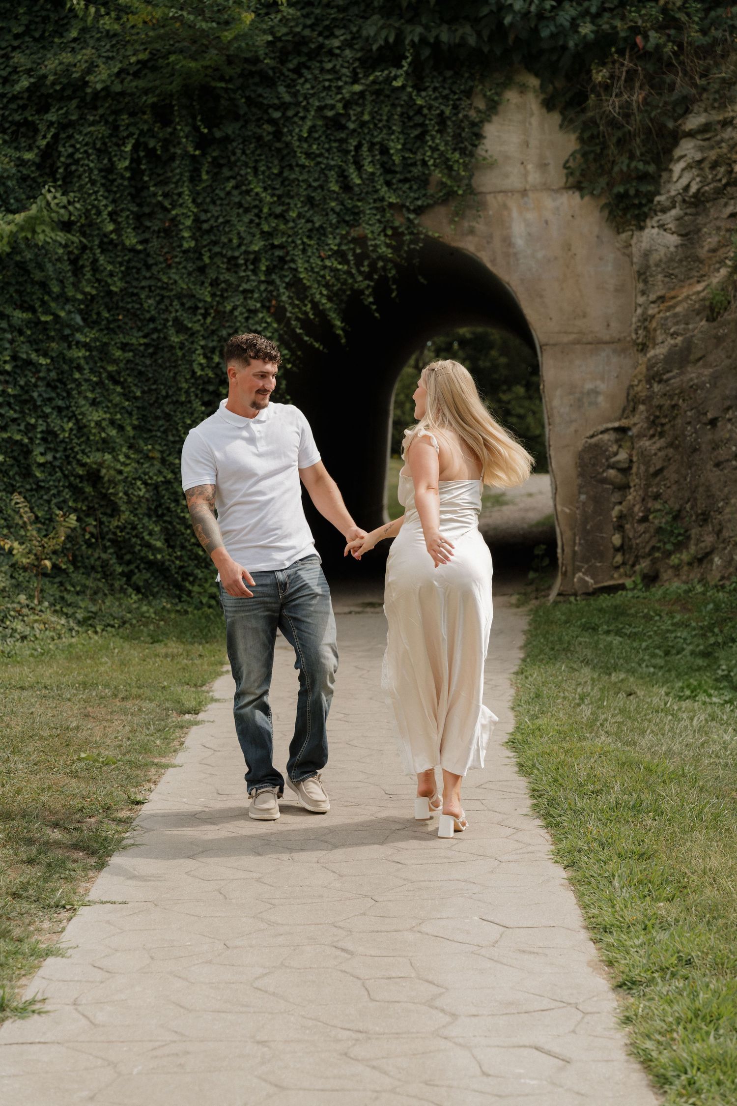 Couple walking away through stone archway covered in ivy.