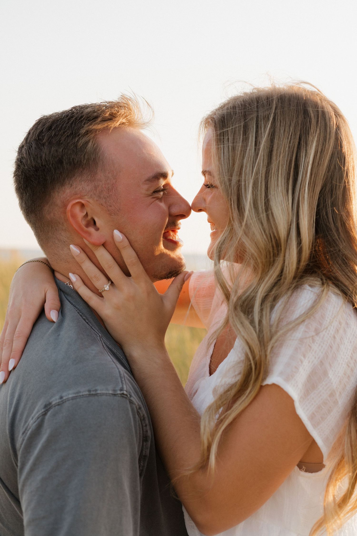 Close up of couple sharing tender moment in warm sunset light with beach grass background.