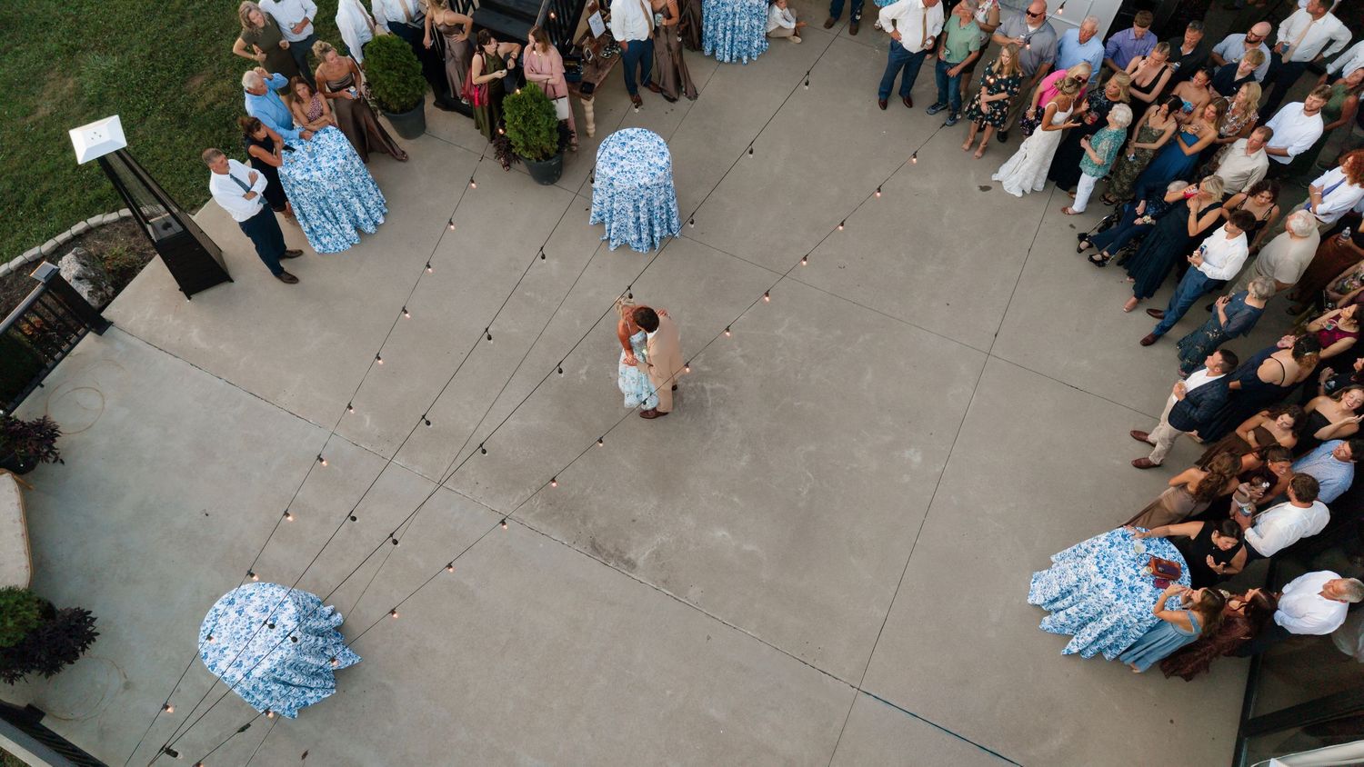 Aerial view of a child releasing balloons at an outdoor celebration surrounded by guests on a paved courtyard.