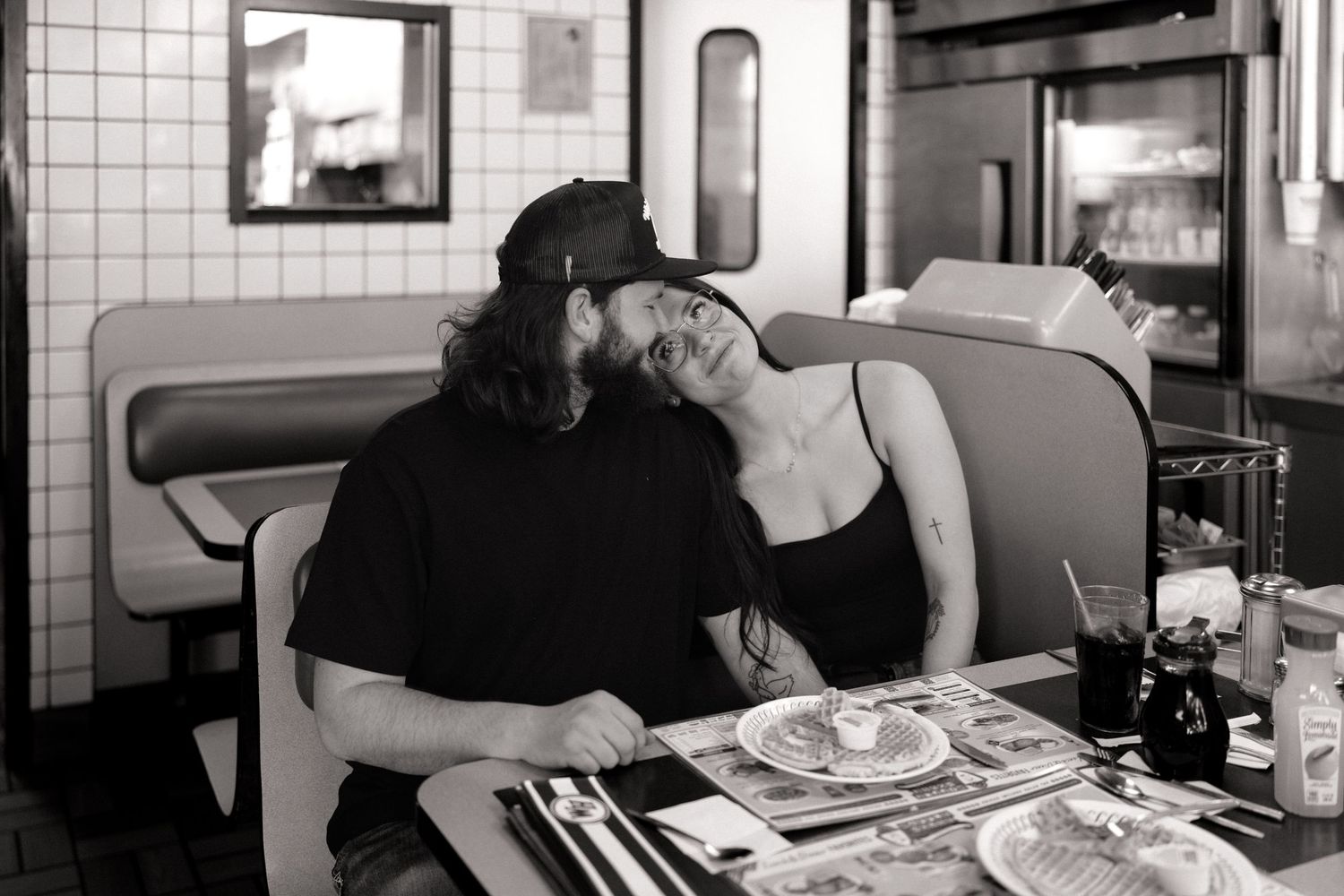 Couple sitting together at a retro diner counter with white tile walls.