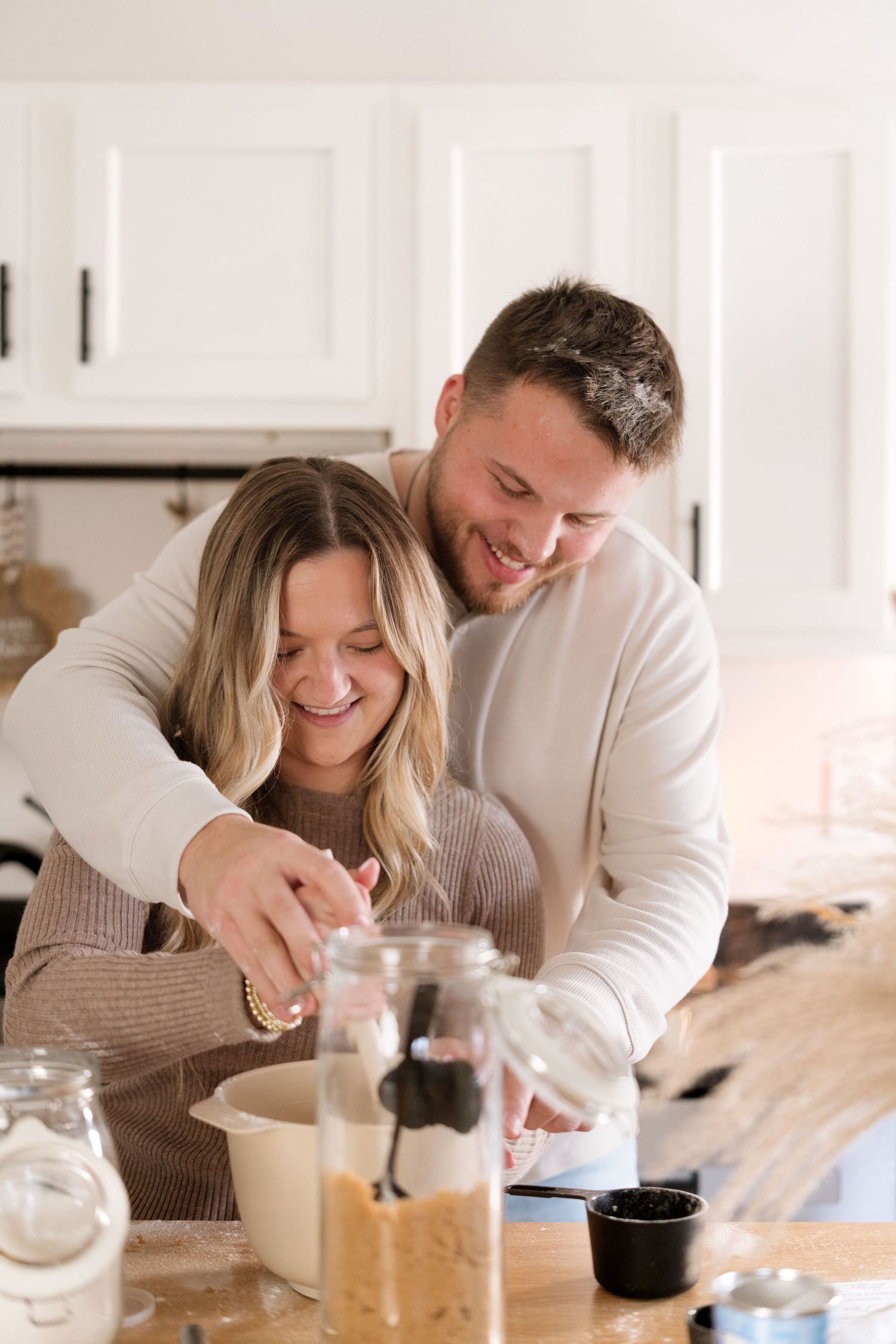 A couple laughs together while enjoying coffee and breakfast at a bright white kitchen counter.