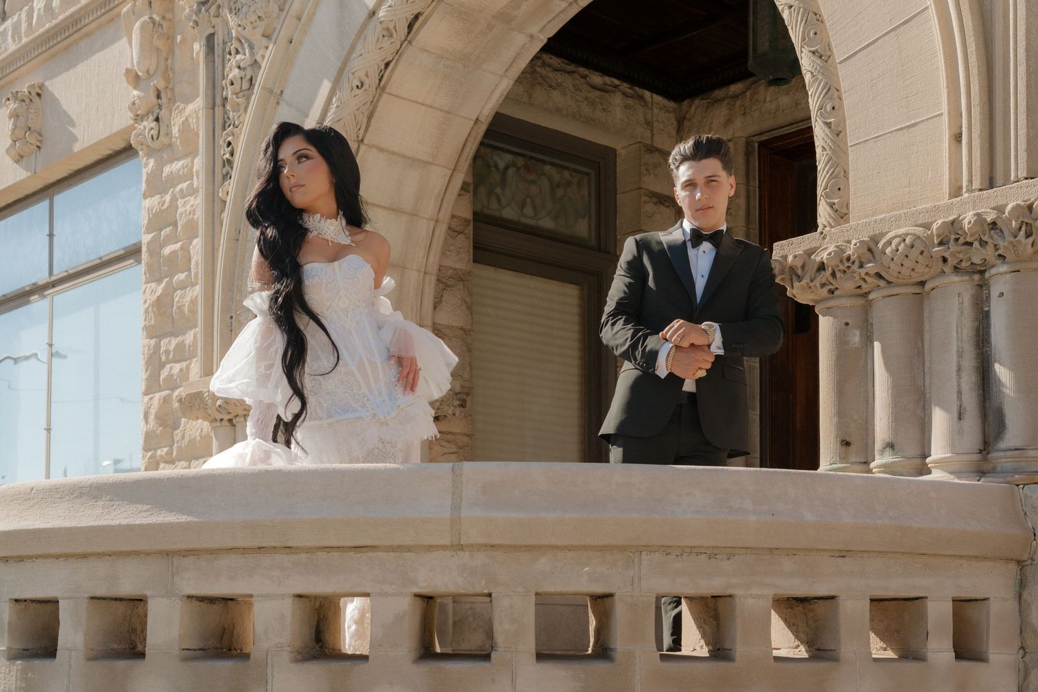 Newlyweds share romantic moments on ornate stone balcony.