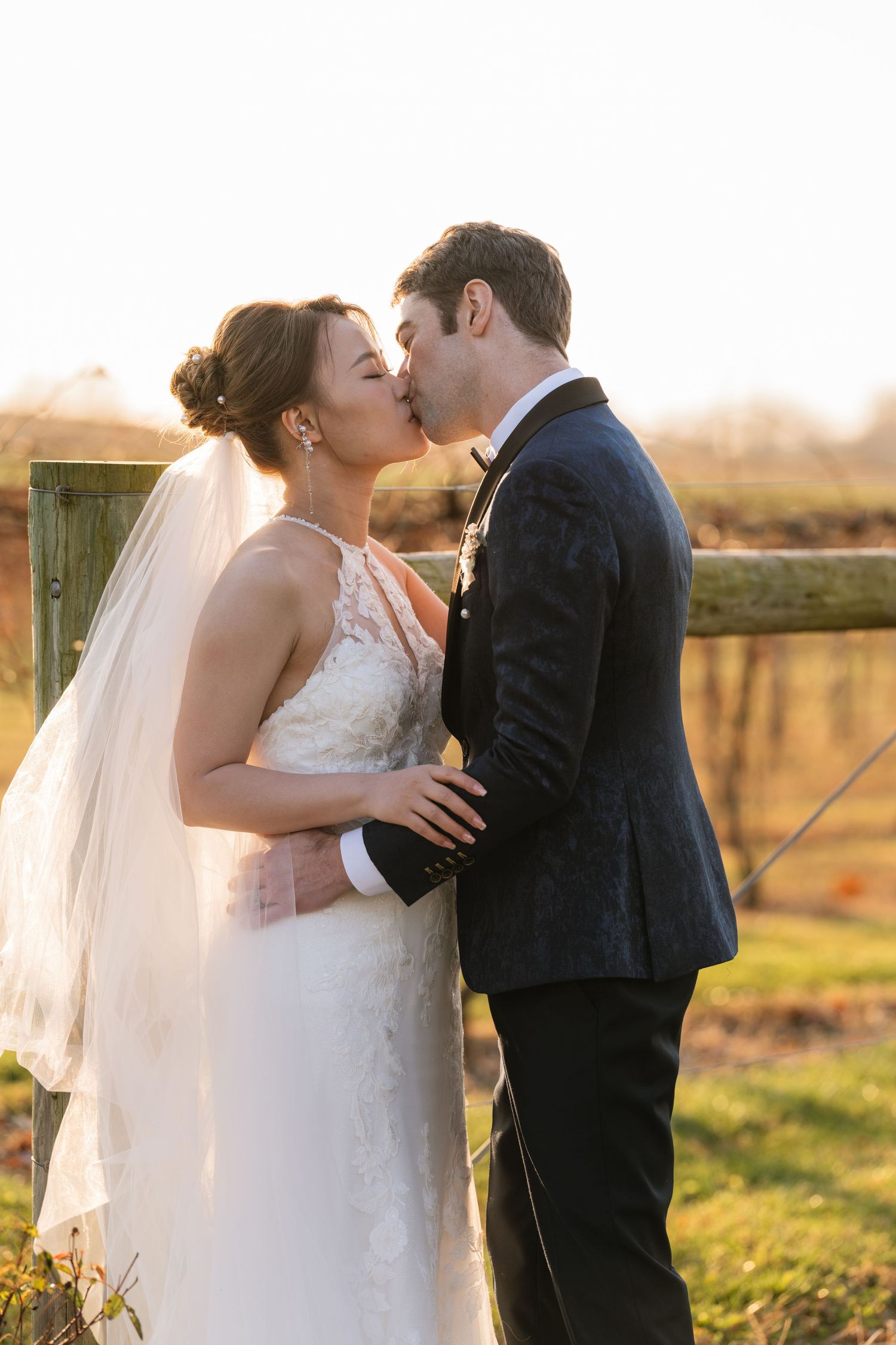 Intimate sunset wedding portrait in front of rustic wooden fence.