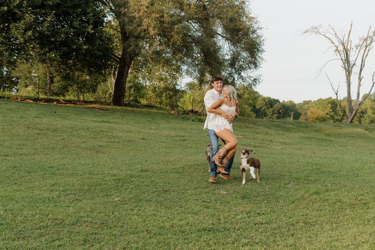 A couple shares a romantic moment on horseback in a sunny green field.