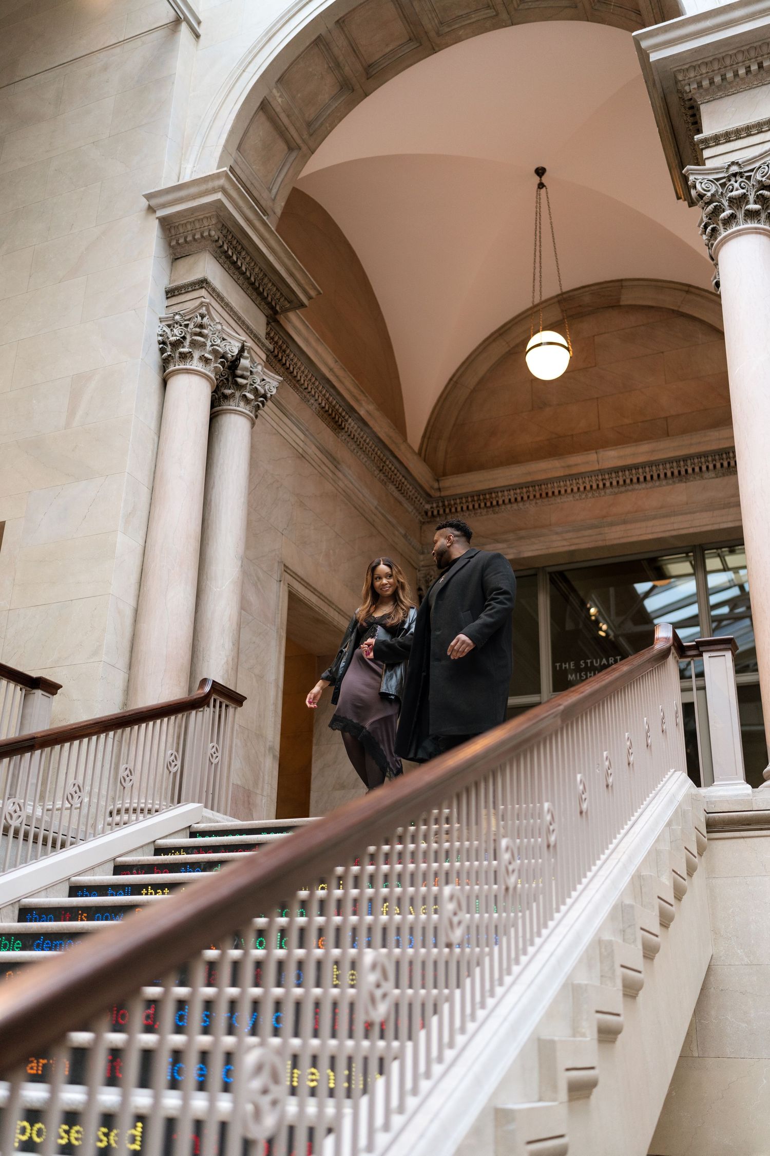 A sequence of four photos showing people walking up an elegant white marble staircase with arched ceilings in a historic building.
