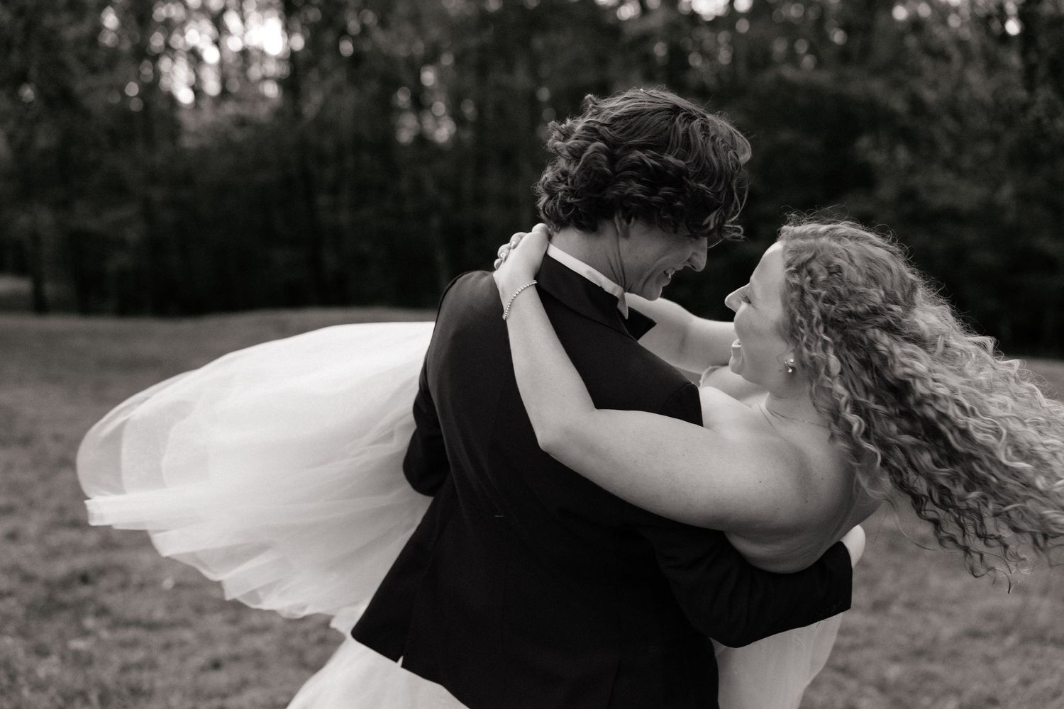 Black and white photo of a bride and groom embracing outdoors, her curly hair and veil flowing in the breeze.