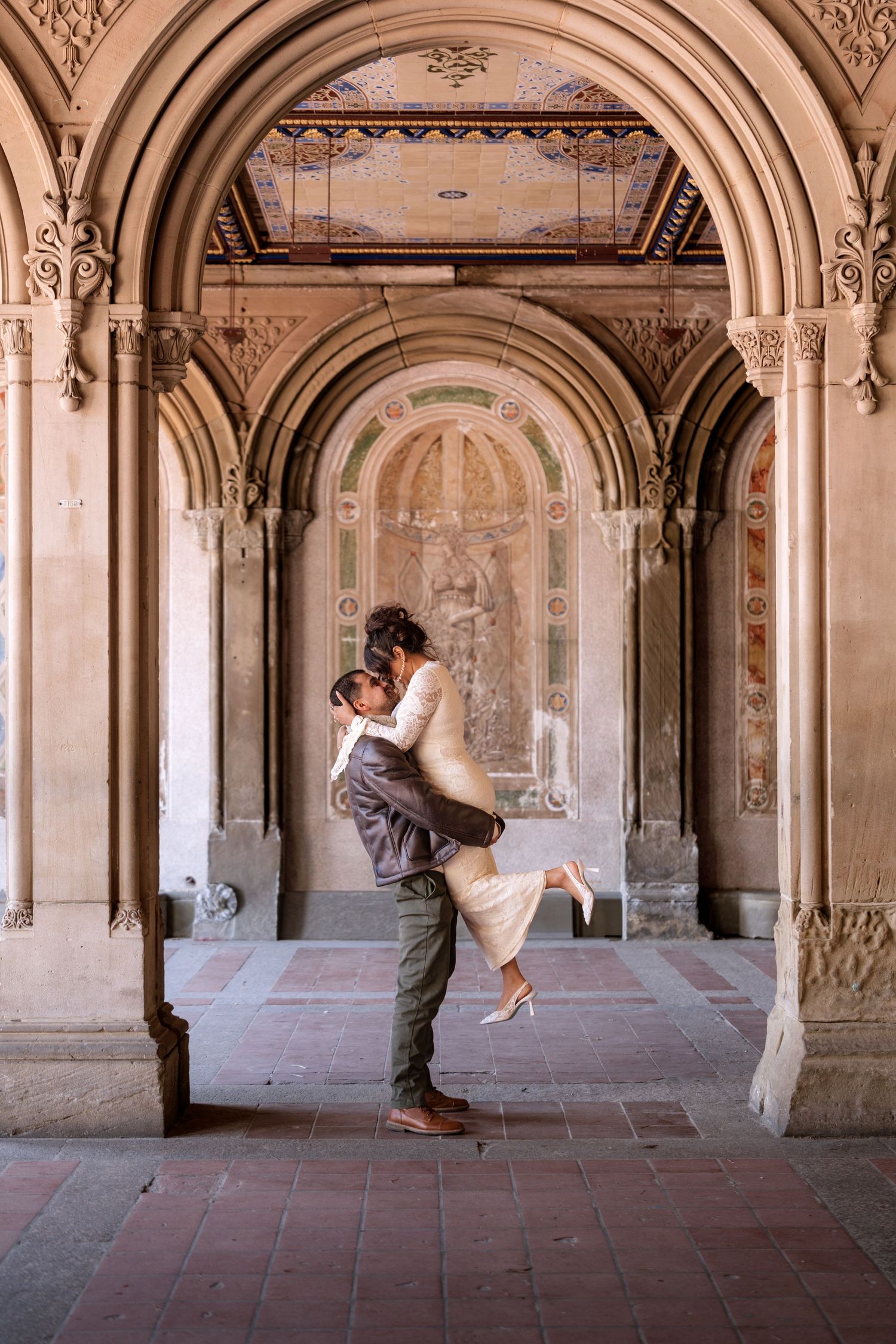 Couple embracing under ornate stone arches at Bethesda Terrace in Central Park, NYC, in a romantic wedding moment.