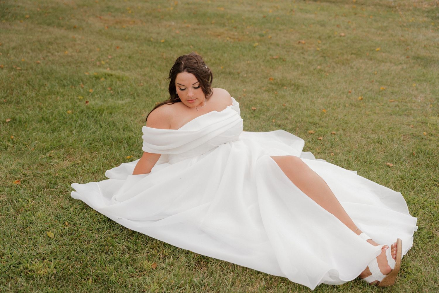 White wedding dress flowing across green grass in outdoor setting.