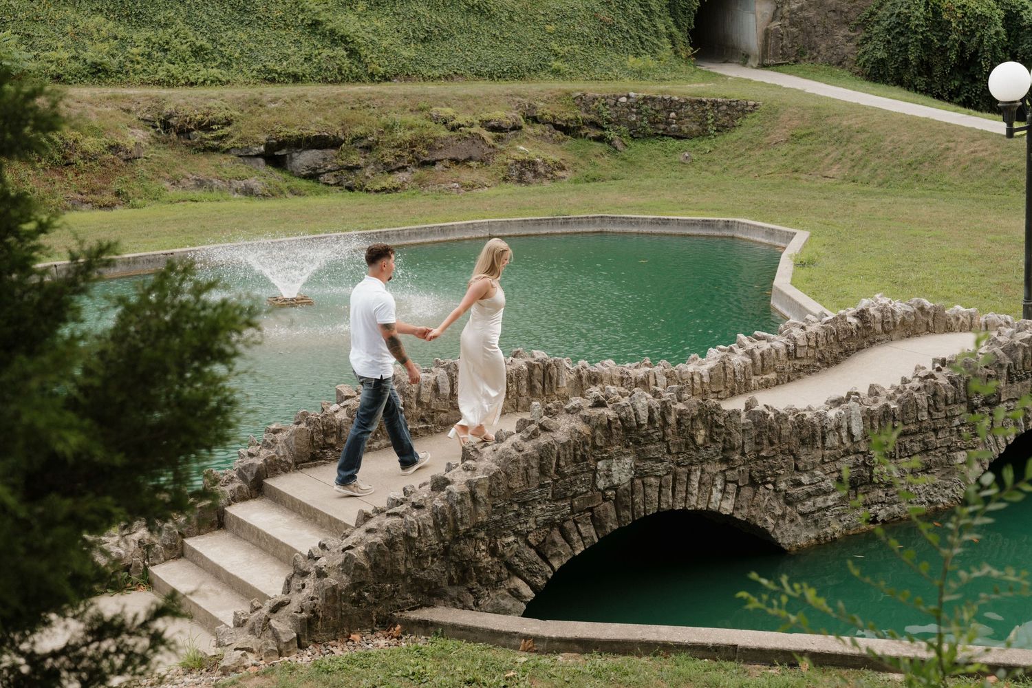 Couple walking across scenic stone bridge over turquoise water.