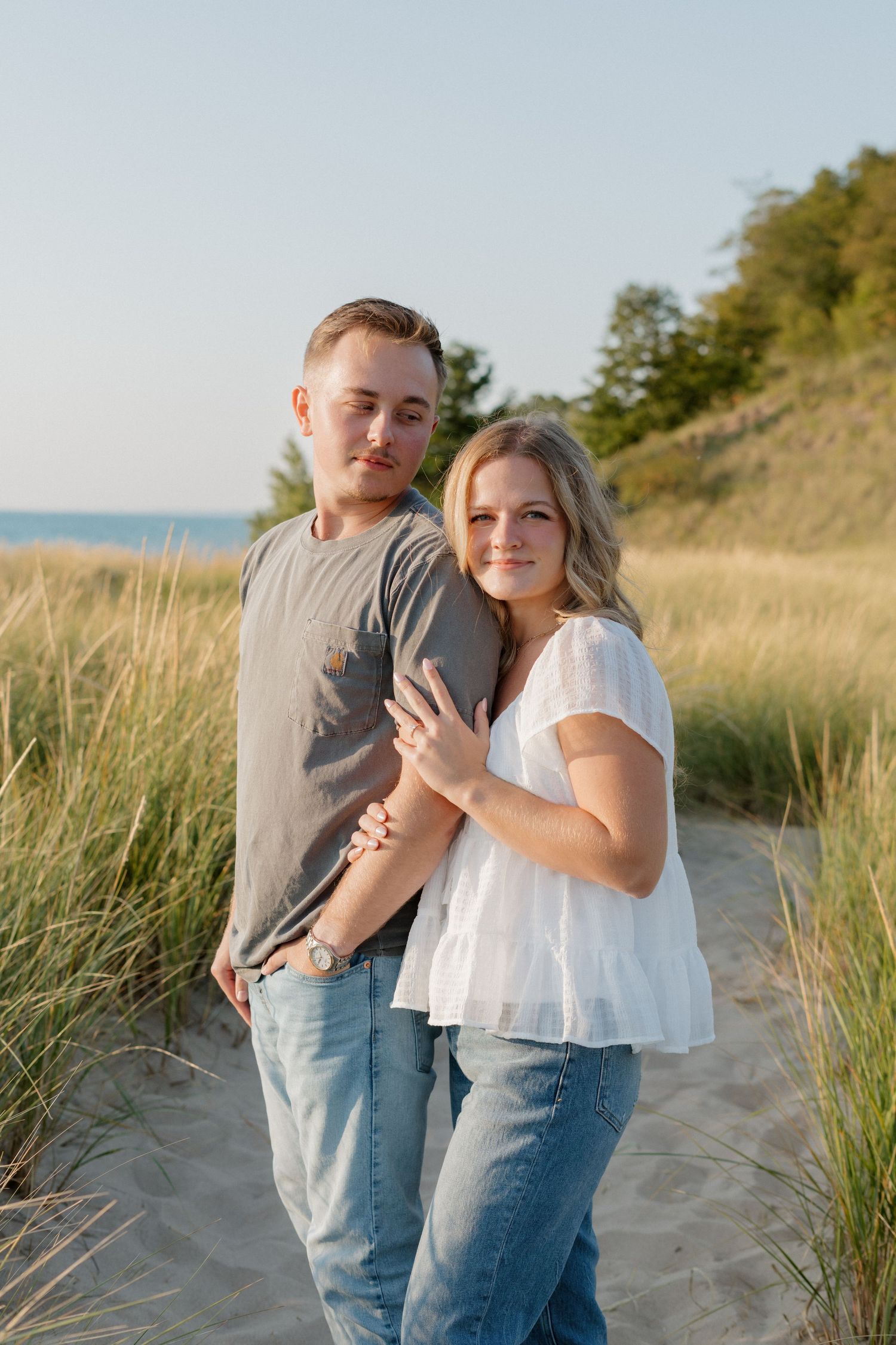 Couple sharing intimate moment on beach path with coastal vegetation and blue sky background.