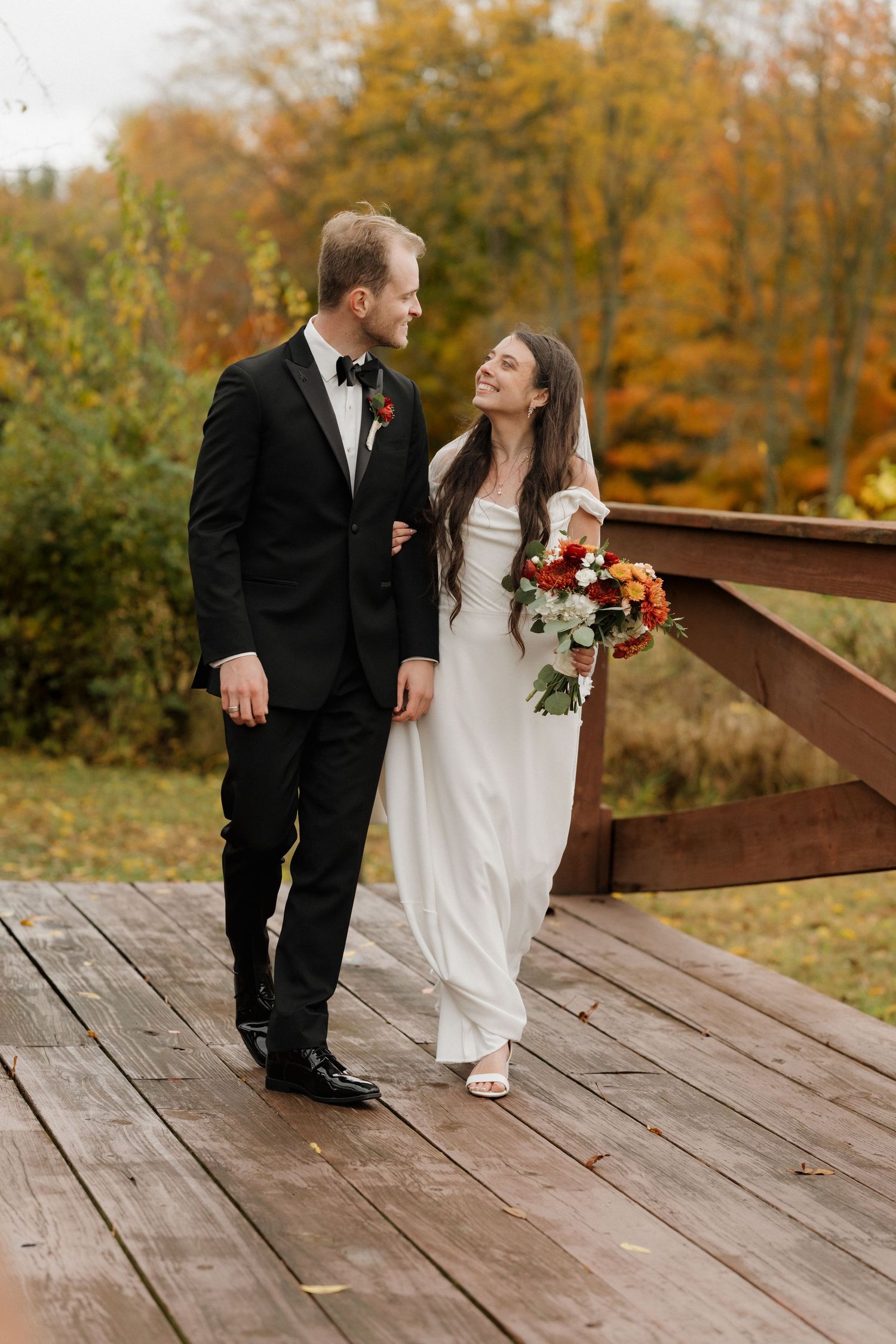 Wedding couple shares intimate moment on rustic wooden deck surrounded by fall foliage.