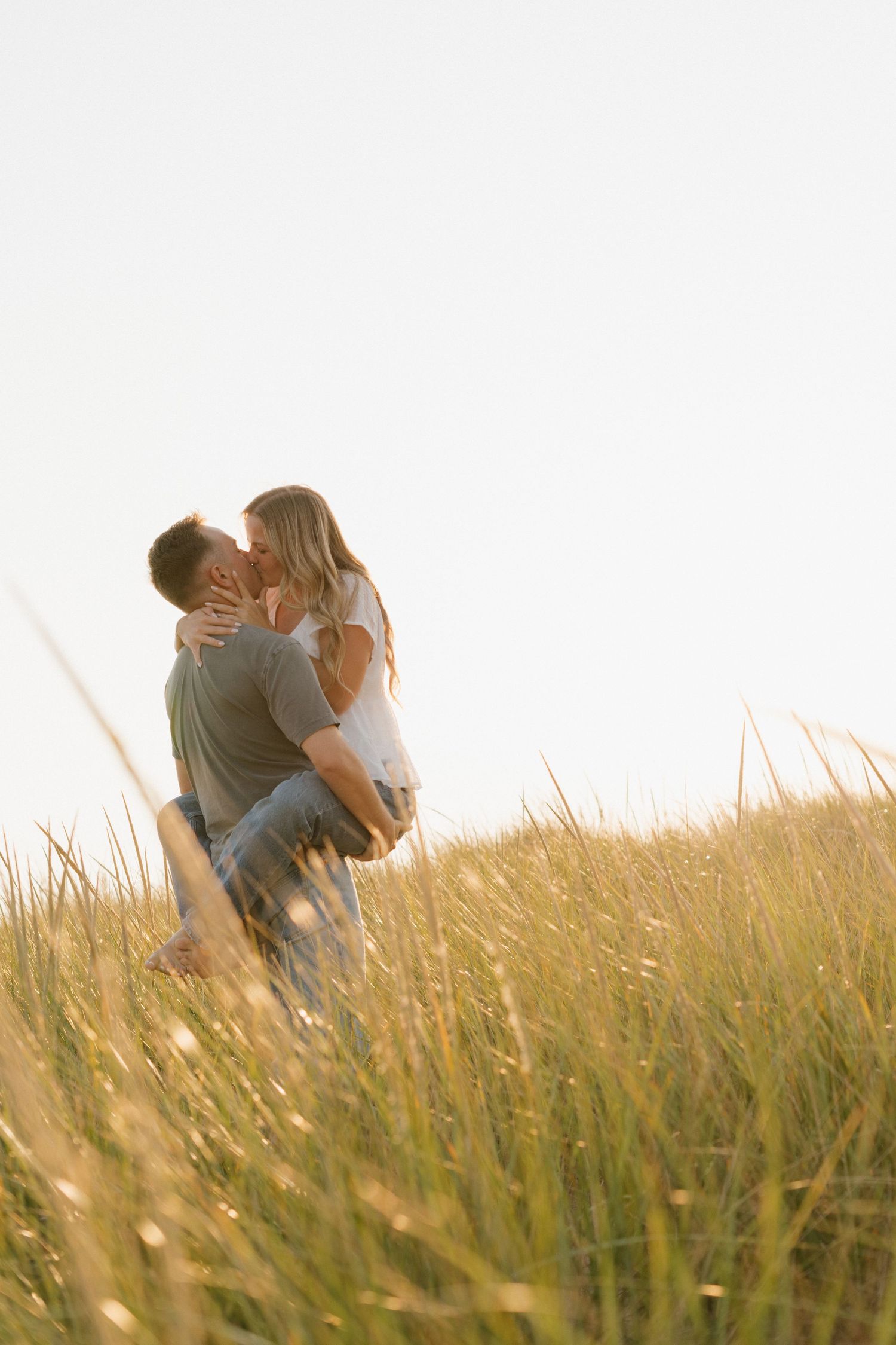 Couple sharing a romantic kiss in a sunlit golden grass field on a clear day.