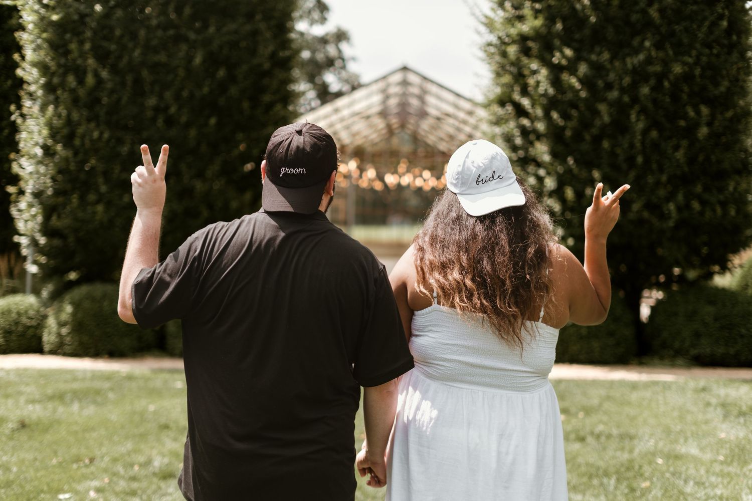Wedding couple holds hands and walks through a lush garden setting during their outdoor celebration.