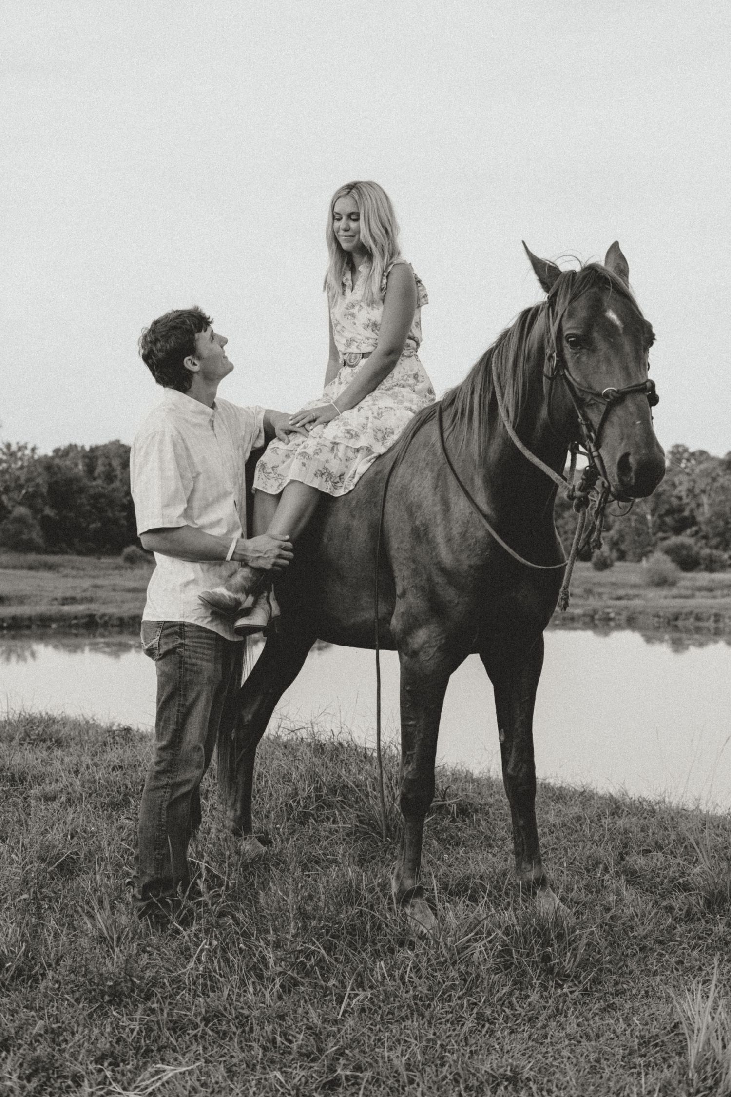 Vintage style black and white photo of a couple with their horse by a lake.