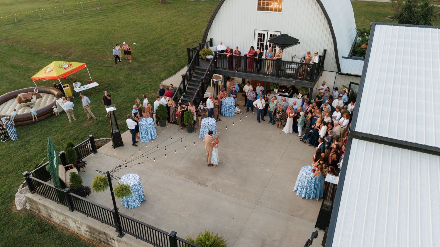 Aerial view of an outdoor wedding reception on a patio beside a barn venue at dusk.