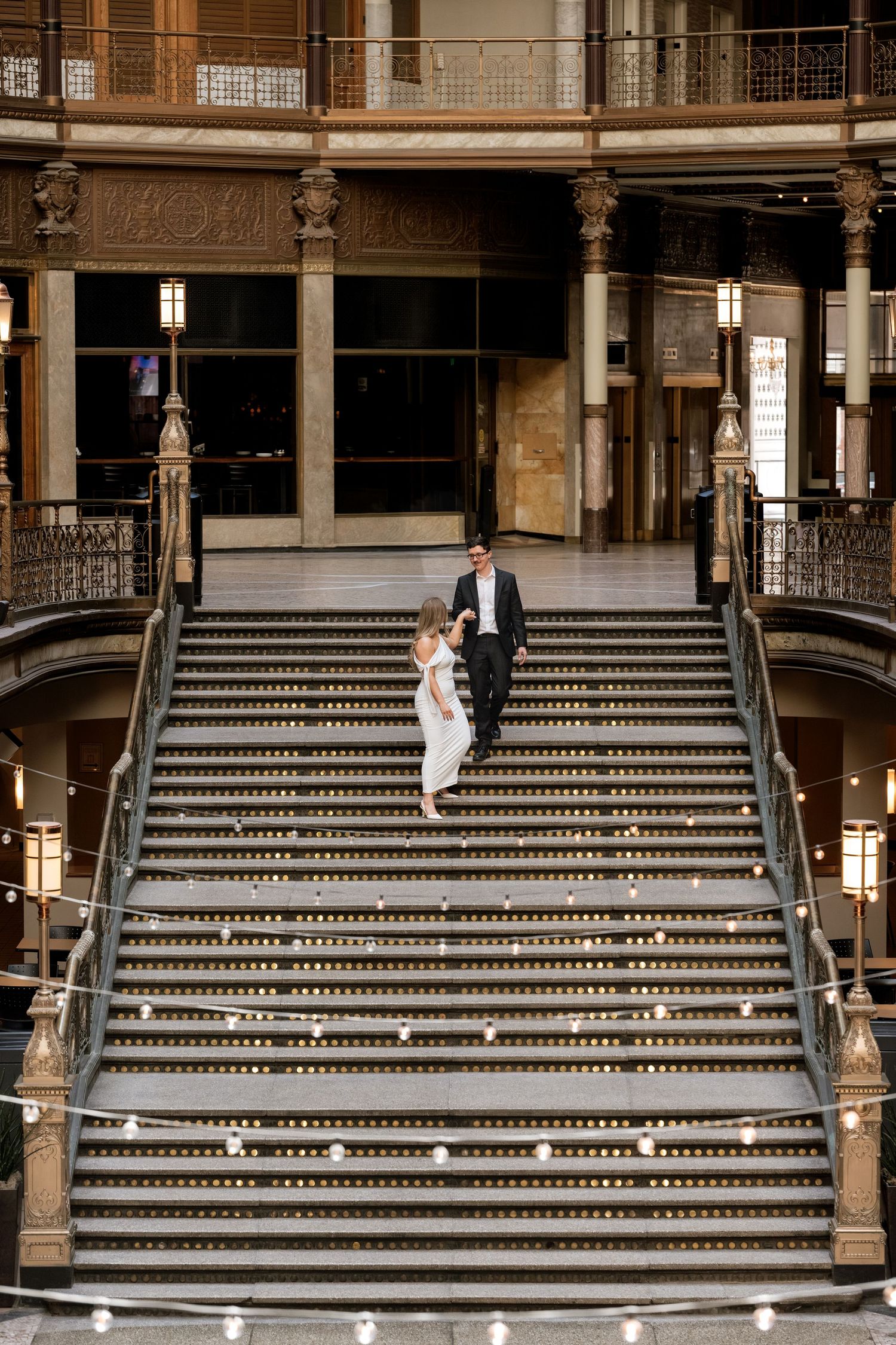 Bride and groom walking down grand staircase in elegant historic building during wedding celebration.