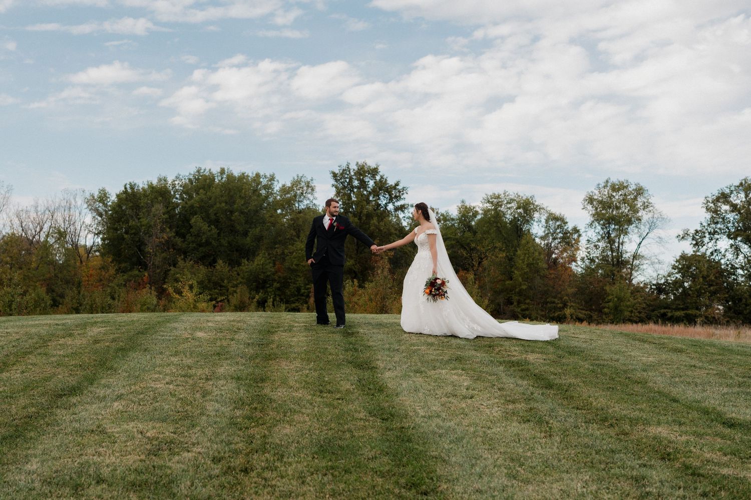 Wedding couple standing on hilltop with dramatic flowing dress and blue sky backdrop.