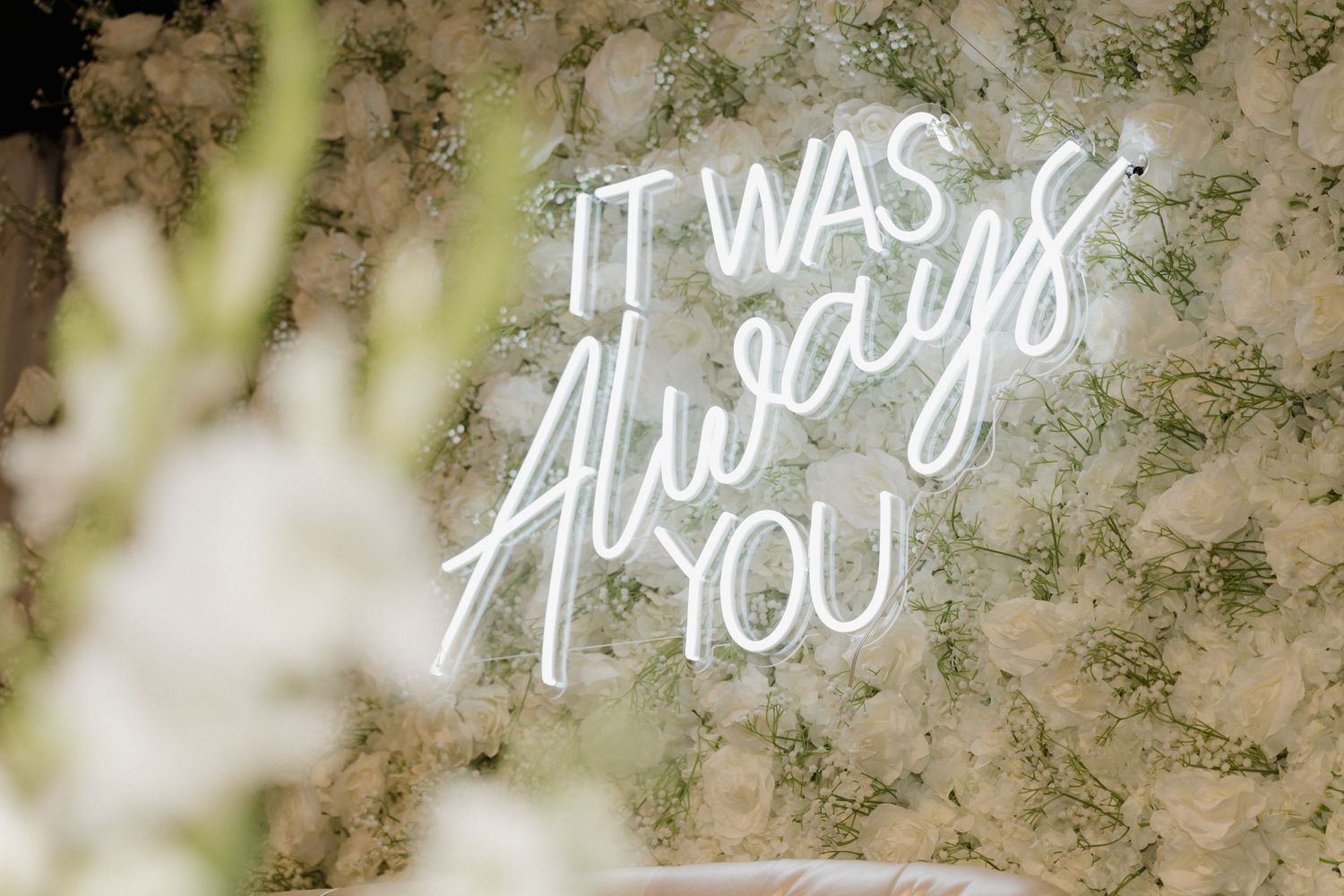 Illuminated neon sign with romantic text displayed against a textured wall.