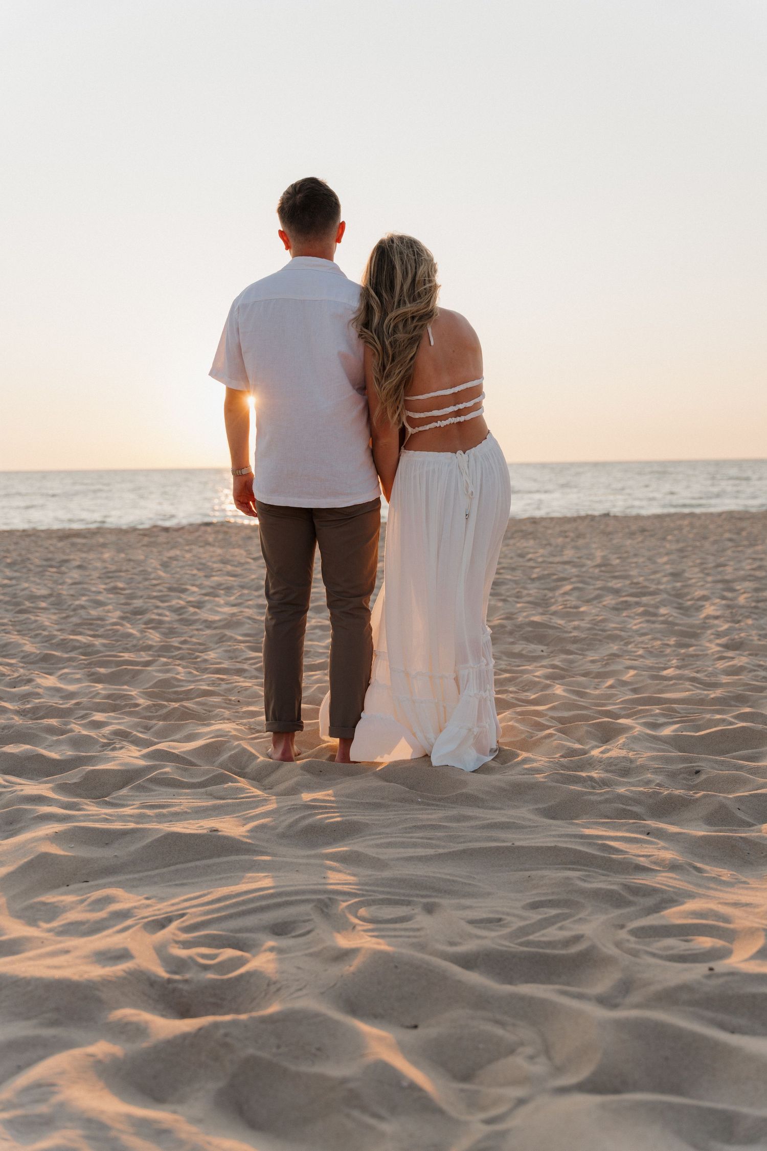 Couple sitting together on sandy beach at sunset watching the water.