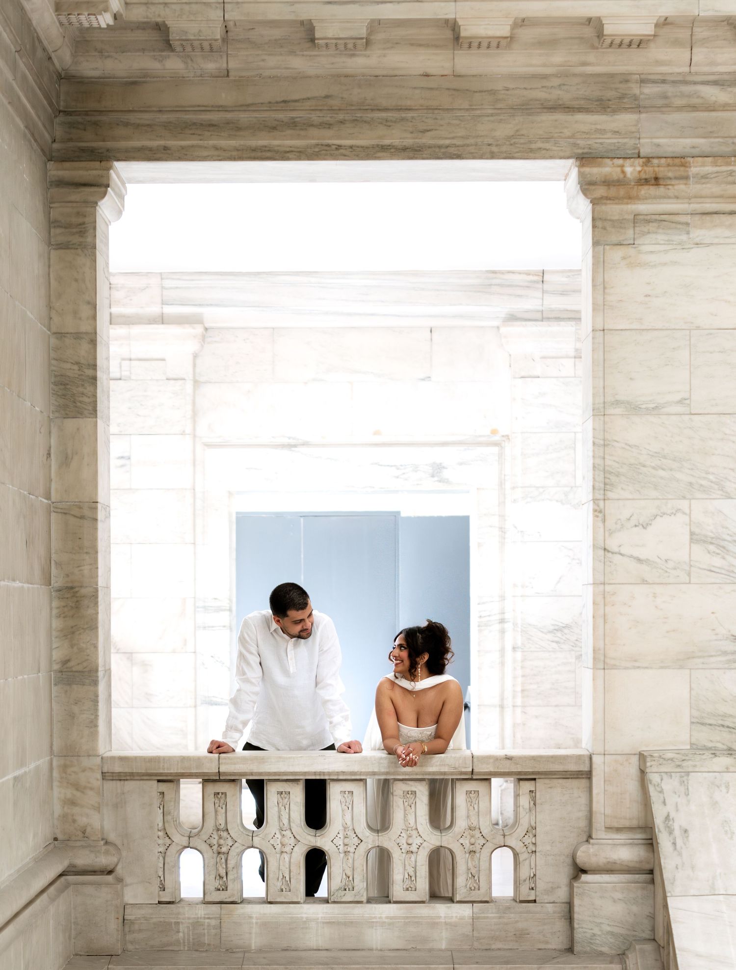 Couple sharing a romantic moment on a marble balcony in an elegant stone building.