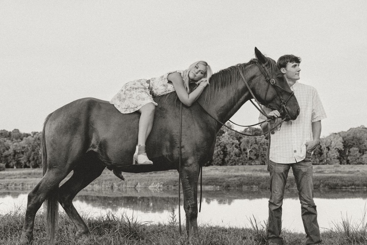 Black and white photo of a couple sharing an intimate moment while sitting on horseback.