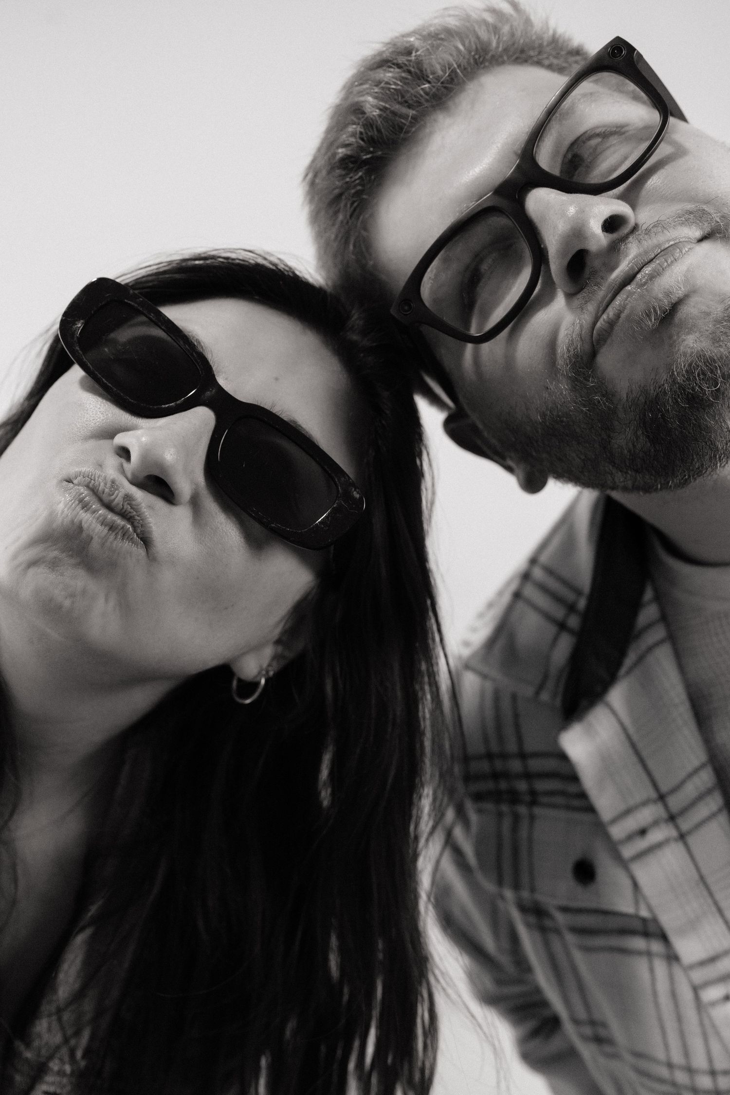 Close-up black and white photo of couple in sunglasses and glasses leaning together.