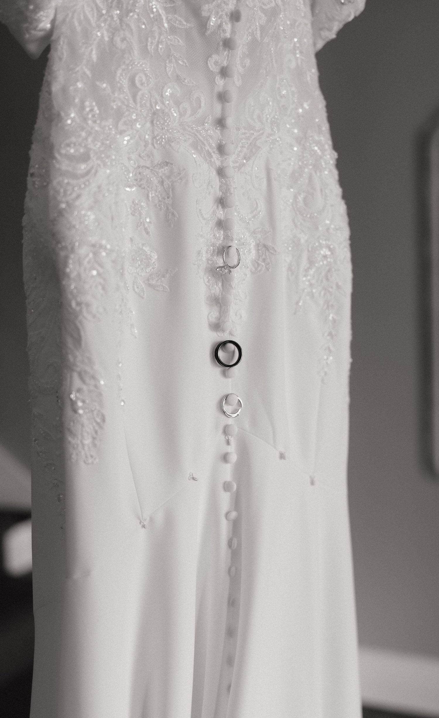 Close-up of an elegant white beaded lace wedding dress with delicate button back closure, hanging gracefully.