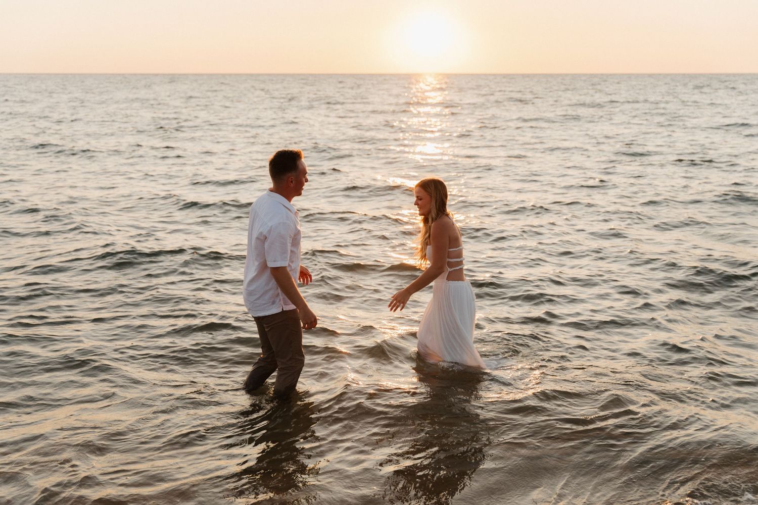 Couple wading in ocean water during golden hour sunset.