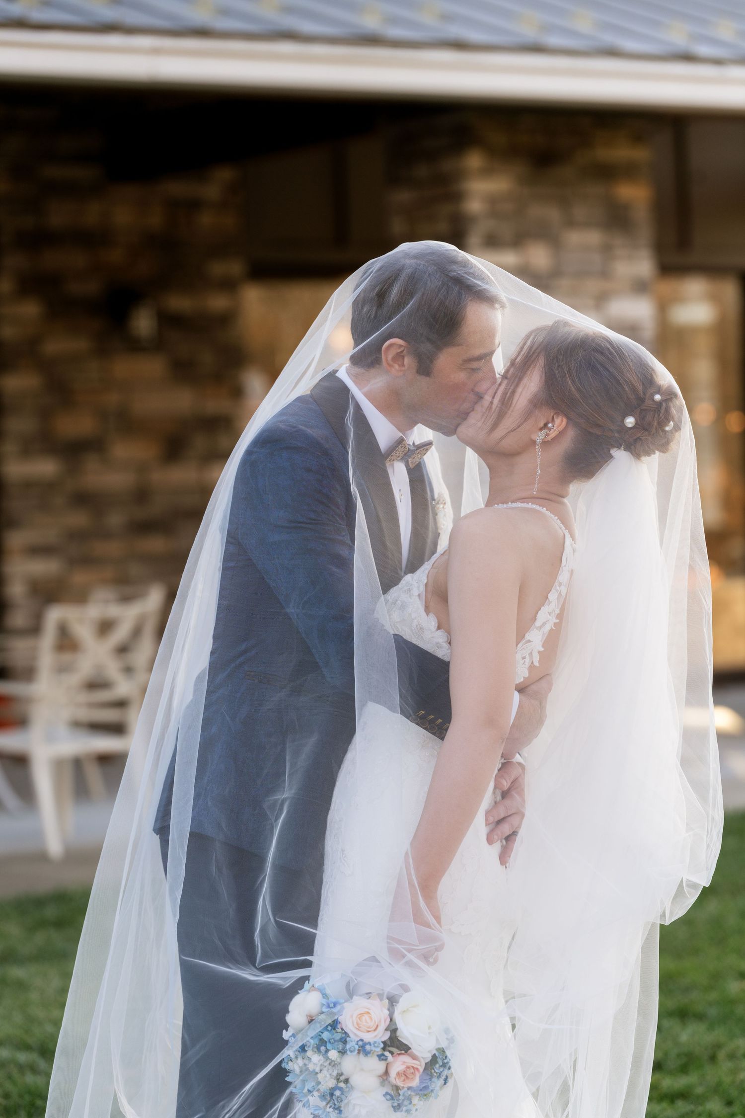 Romantic wedding moment with bride holding pastel bouquet under flowing veil at outdoor venue.