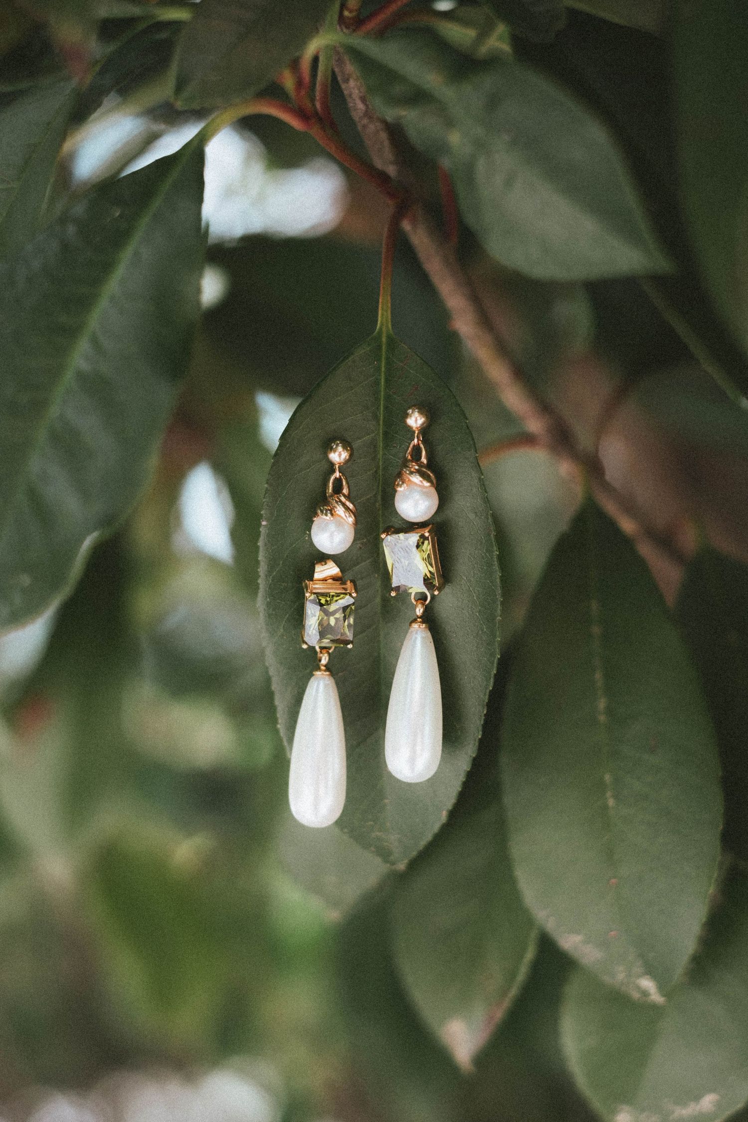 Elegant gold drop earrings with pearl and gemstone details displayed on green leaves outdoors.