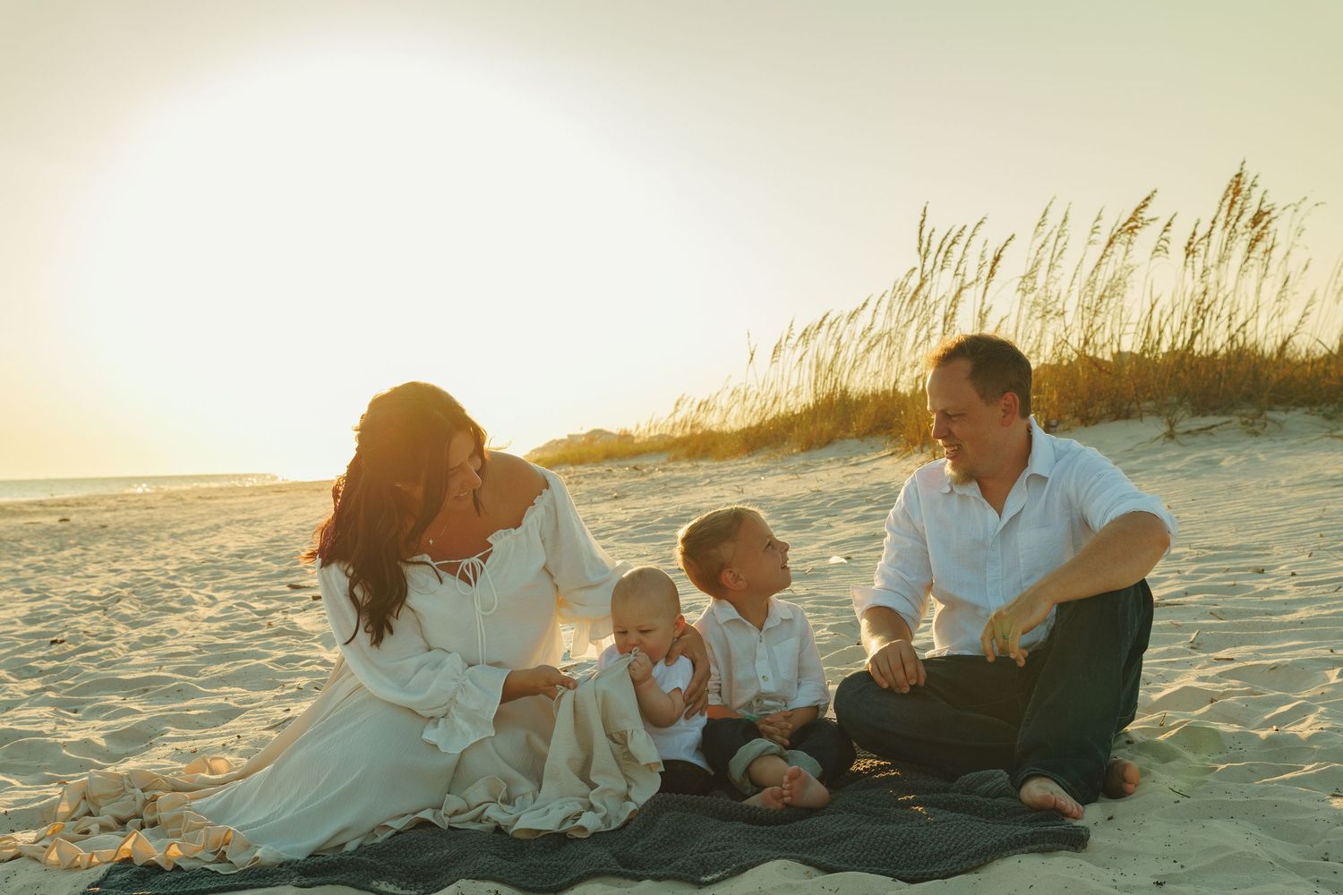 Family relaxing together on sandy beach at sunset.