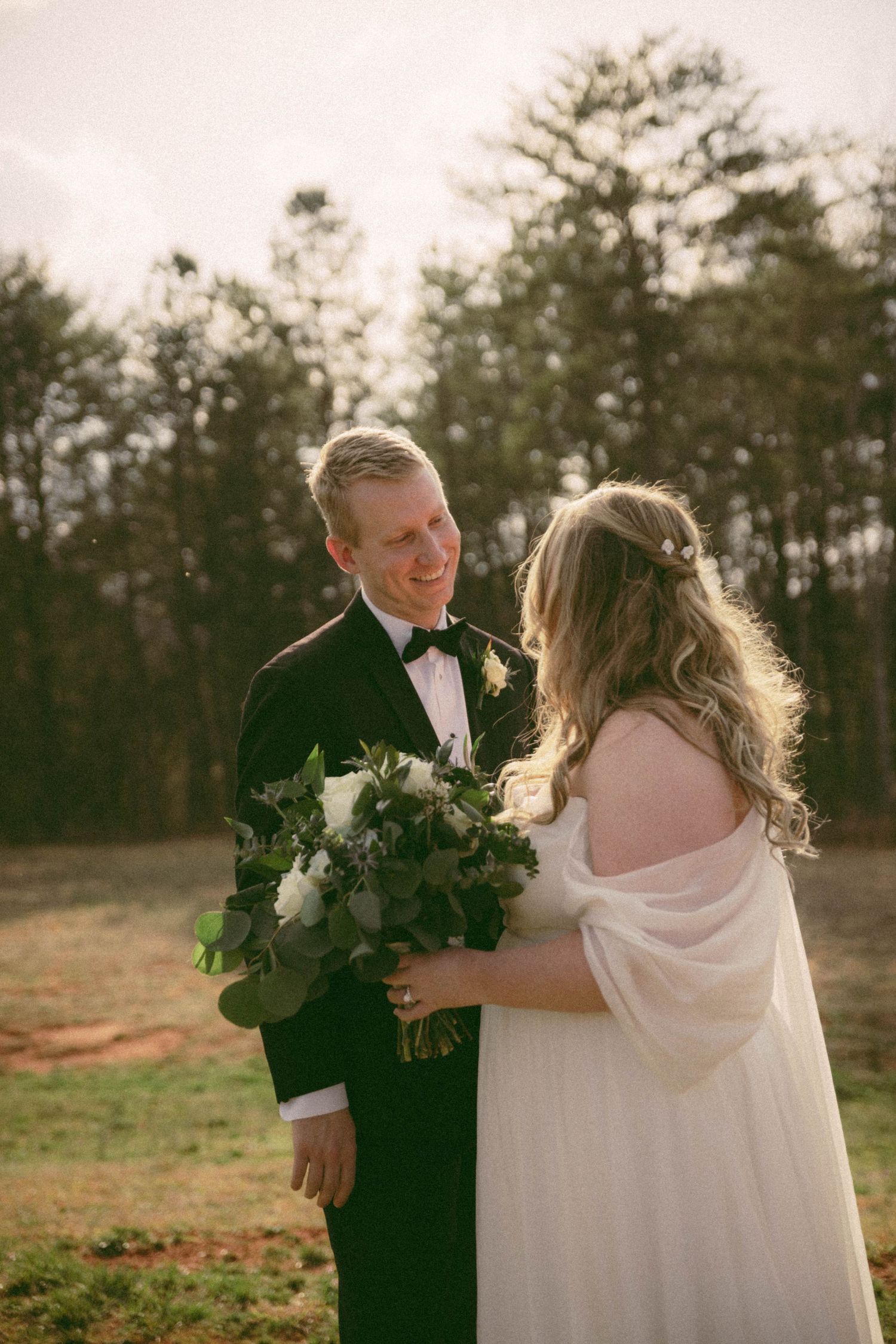Couple sharing an intimate moment at sunset with greenery bouquets.