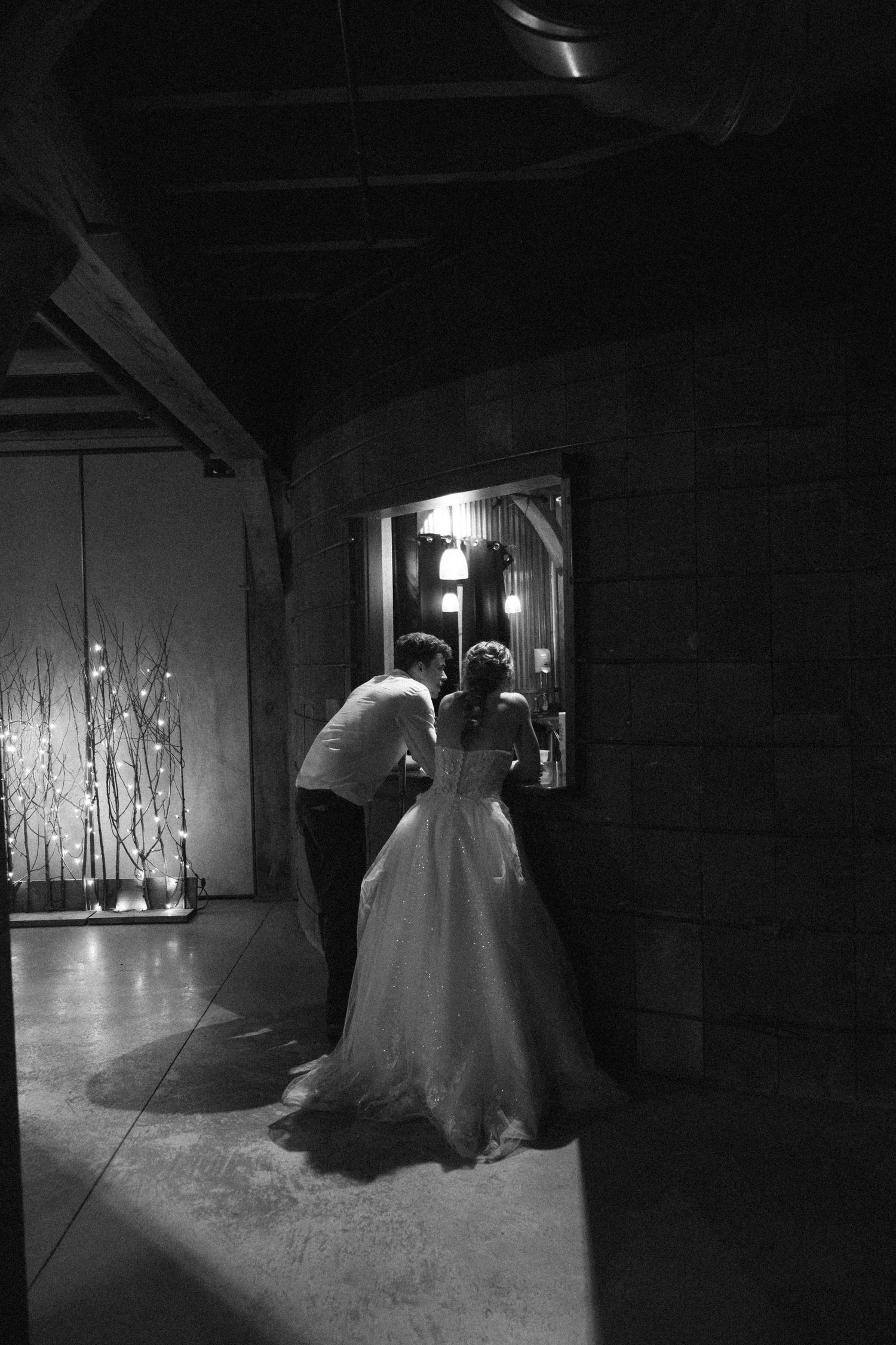 Black and white photo of bride in ball gown and groom sharing intimate moment in dimly lit rustic venue.
