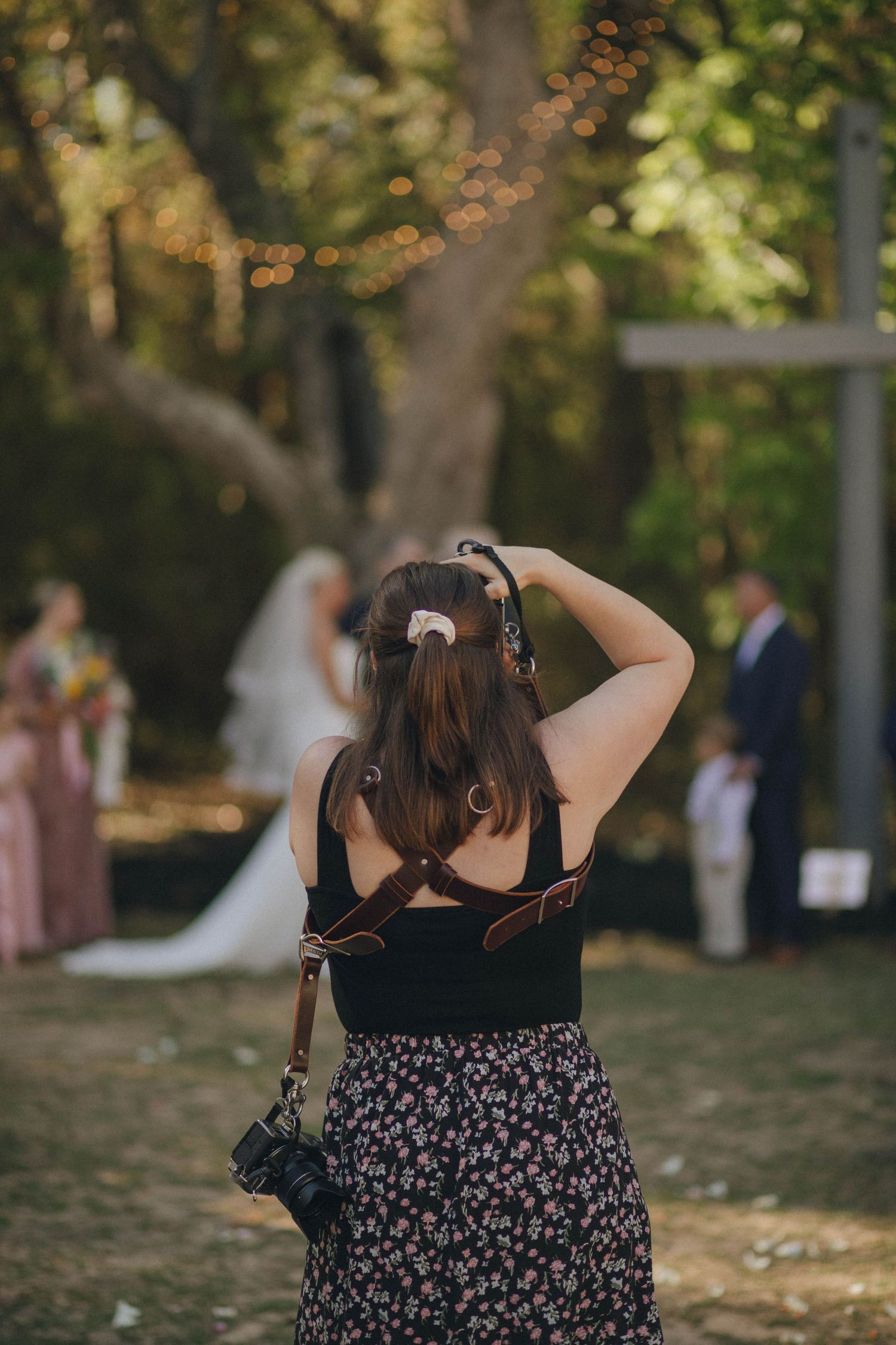 A photographer in a floral dress taking pictures at an outdoor event.