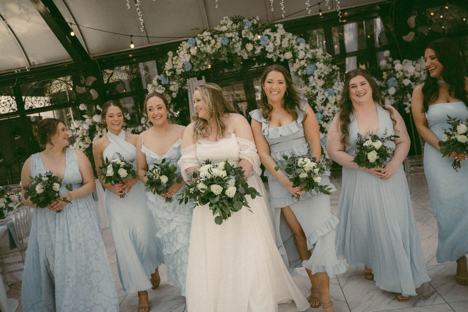 Wedding party in light blue dresses posing with floral arrangements.