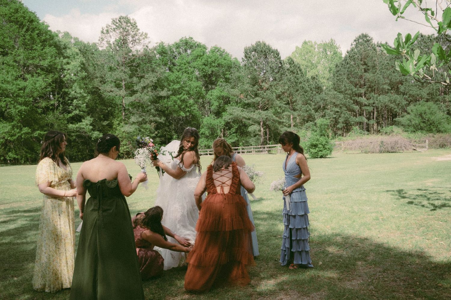 A wedding celebration takes place outdoors in a lush green setting with guests gathered on the lawn.