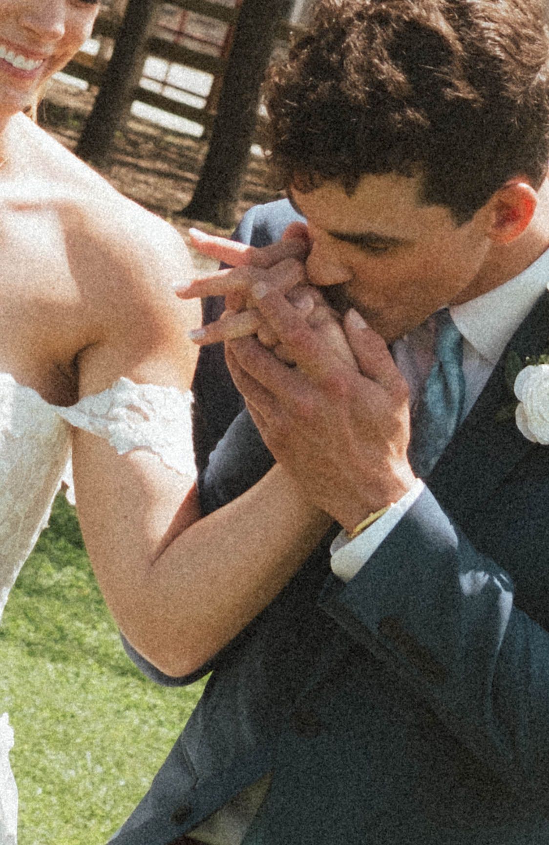 Groom in blue suit kissing bride's hand at outdoor wedding ceremony.