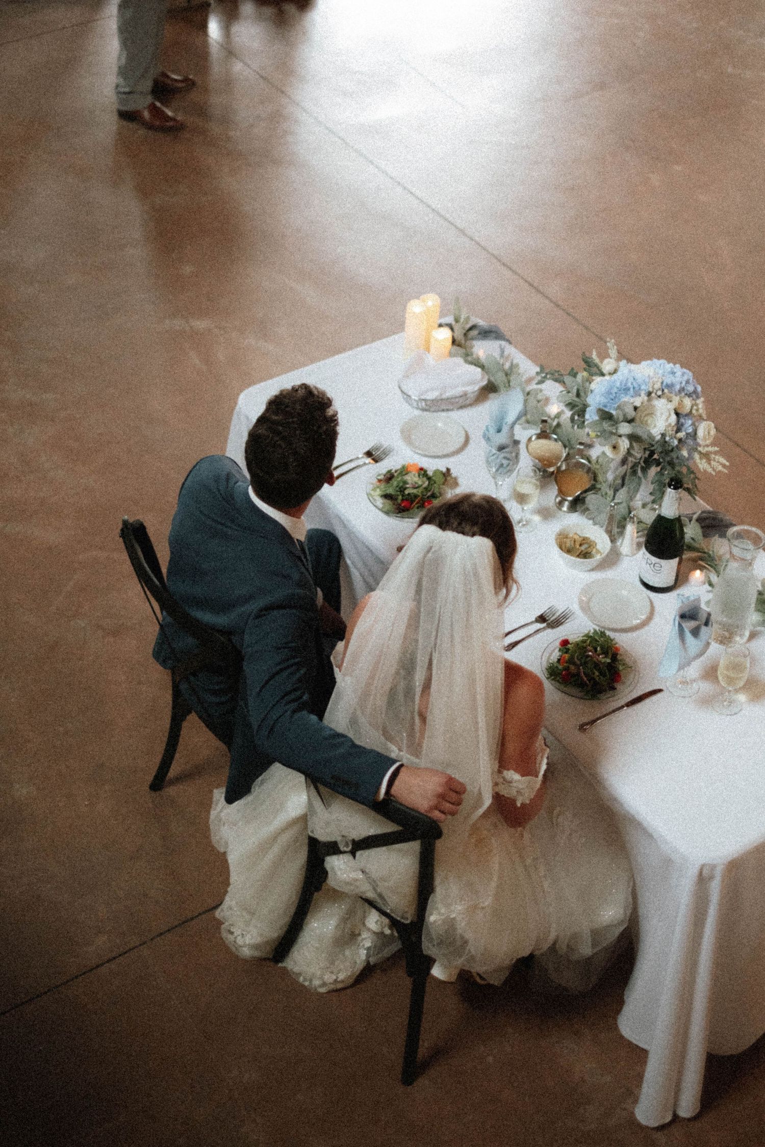 Aerial view of bride and groom seated at candlelit sweetheart table with blue florals.