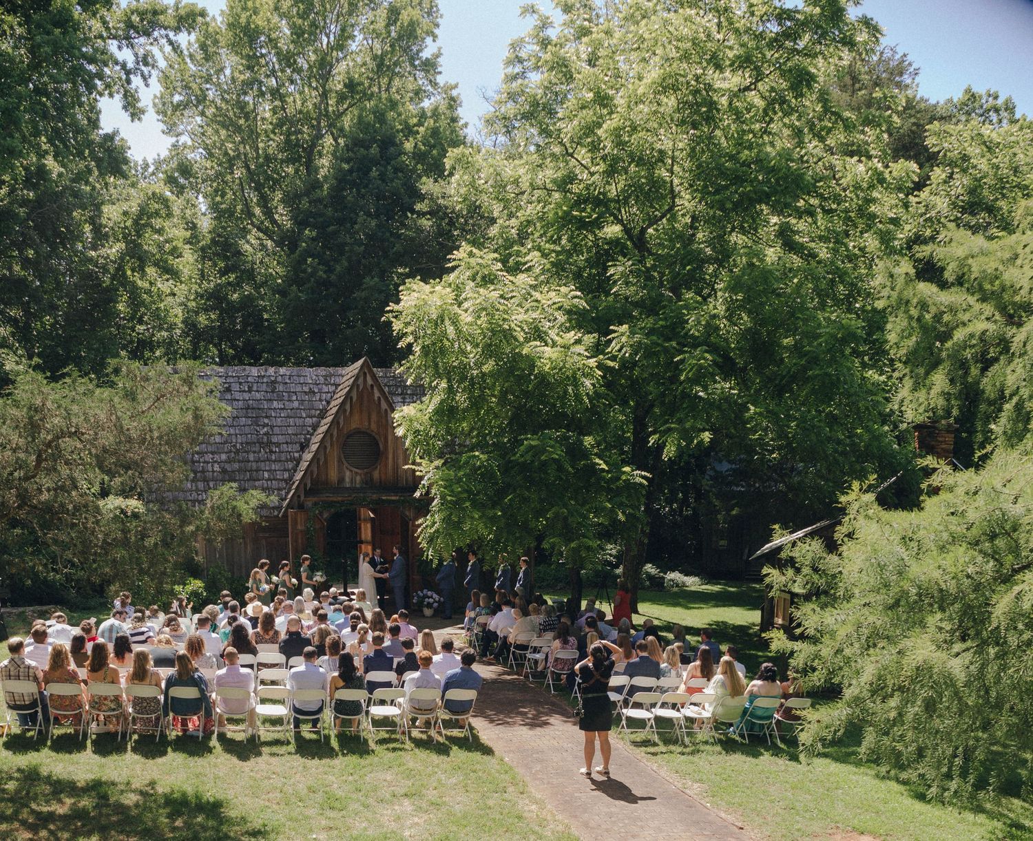 Outdoor wedding venue with wooden chairs set up on grass surrounded by trees.