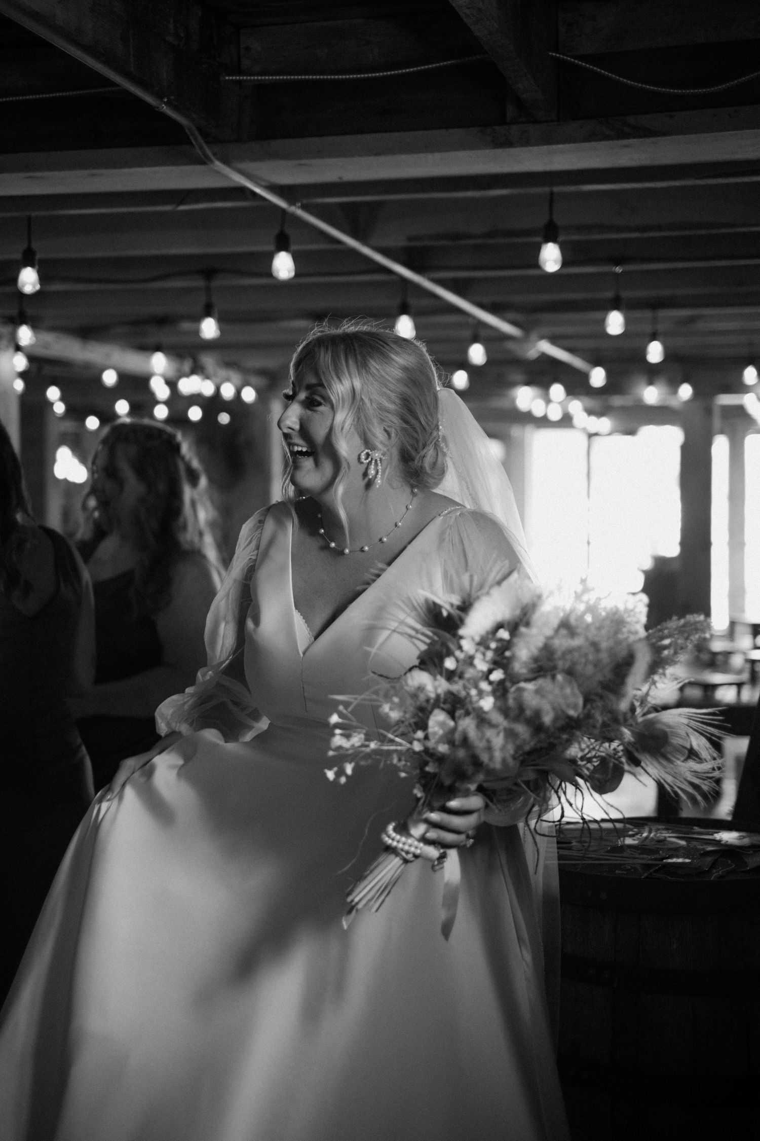 Black and white photo of bride in elegant gown holding bouquet under string lights.