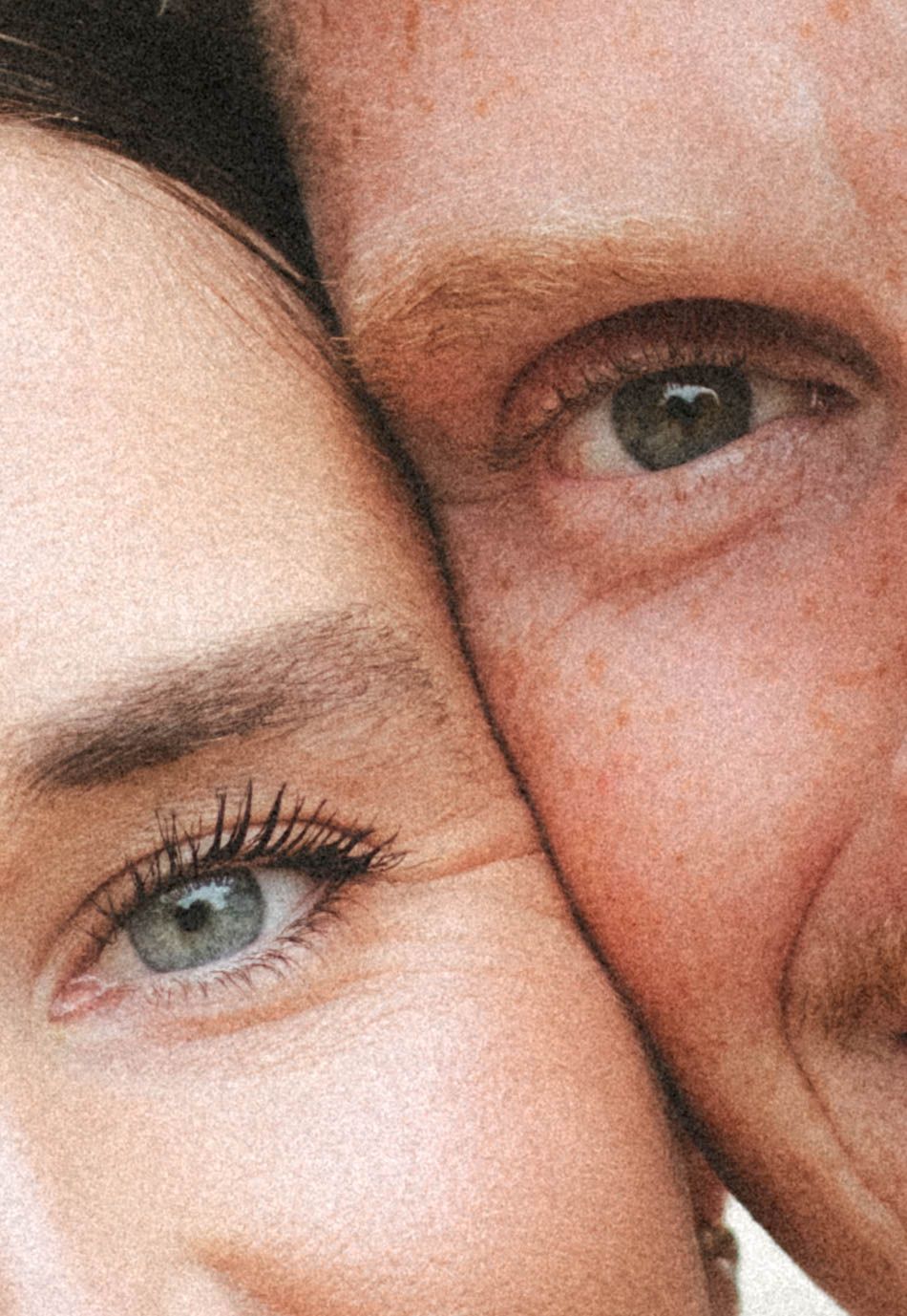 Close-up portrait of two people with striking green eyes and flawless skin pressed cheek to cheek.