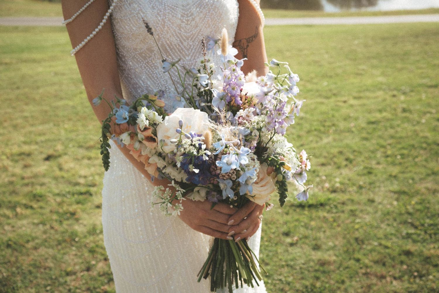 Bride in white gown holding a romantic bouquet of blue, pink, and white wildflowers at an outdoor wedding.