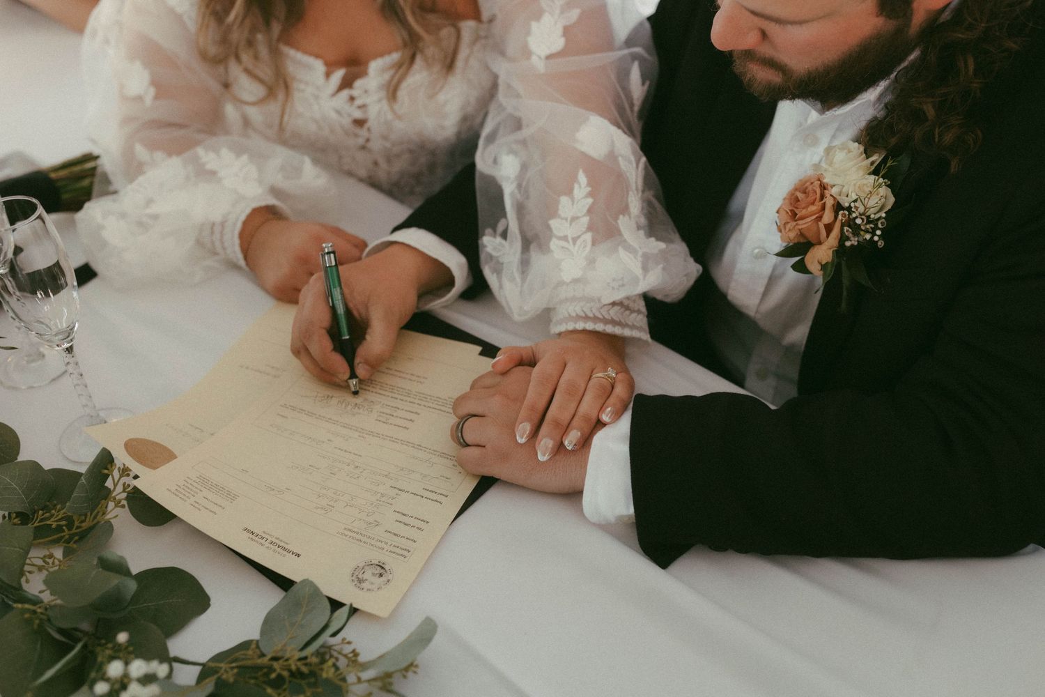 Close-up of hands signing wedding documents on a wooden surface.