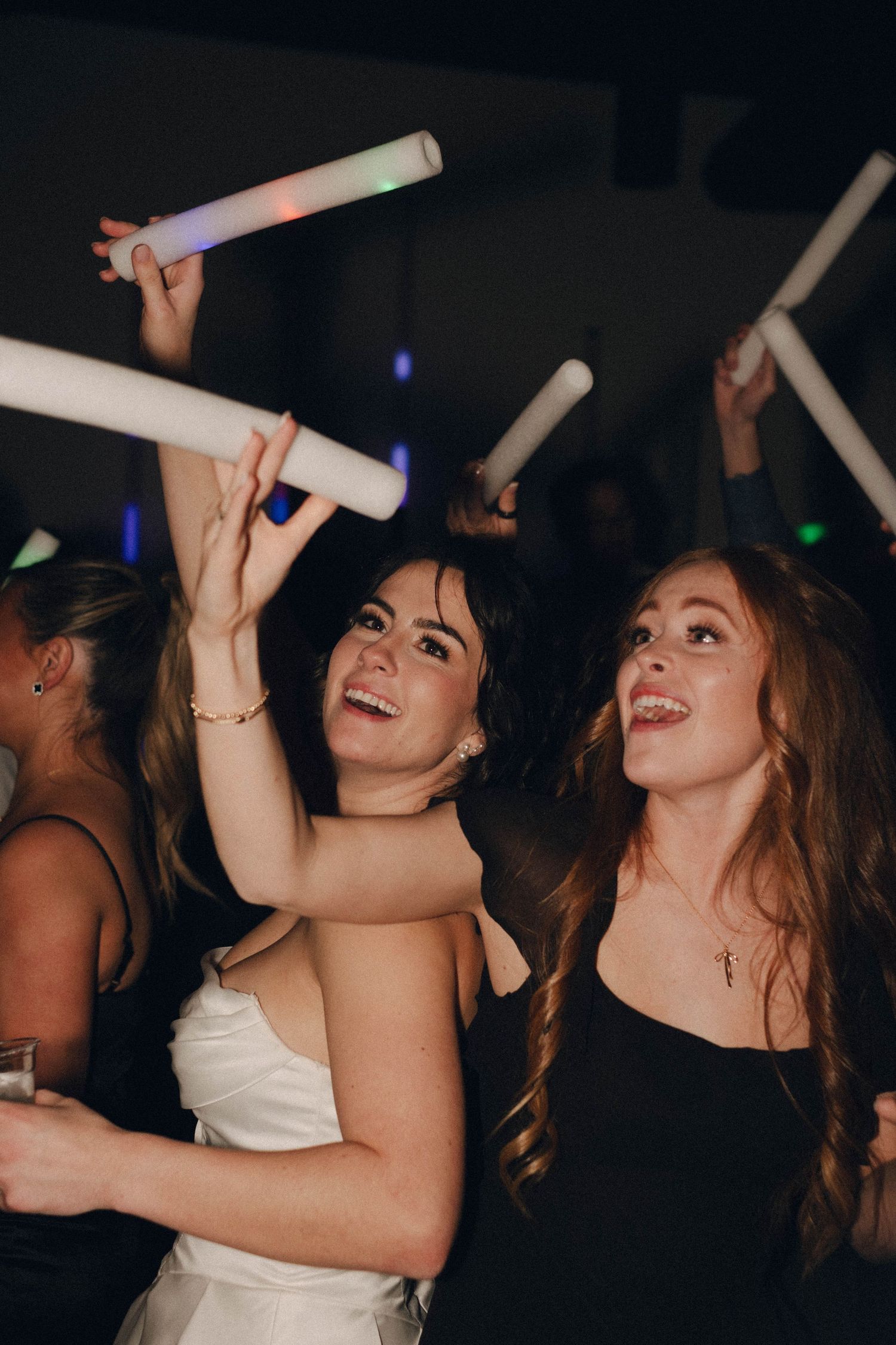 Party guests dance and celebrate with glow sticks in a dark nightclub setting.