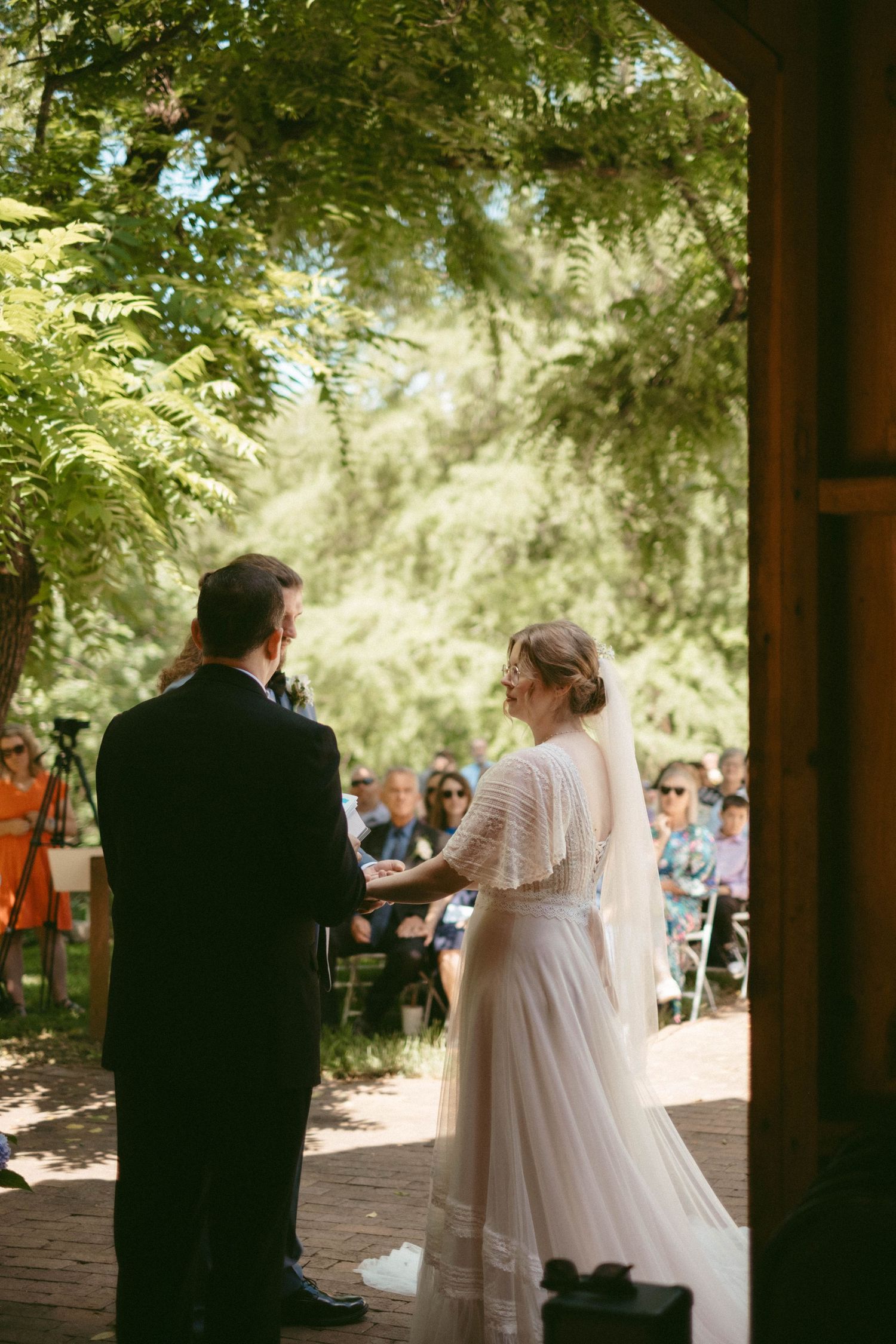 Outdoor wedding ceremony under a wooden pavilion surrounded by trees.