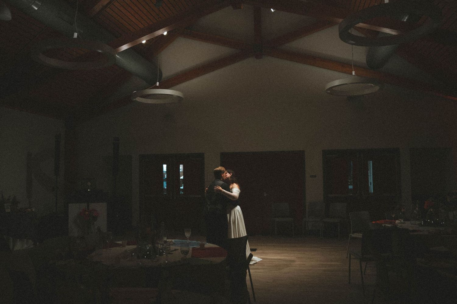 Couple sharing a romantic first dance in a dimly lit reception hall with wooden beam ceiling.
