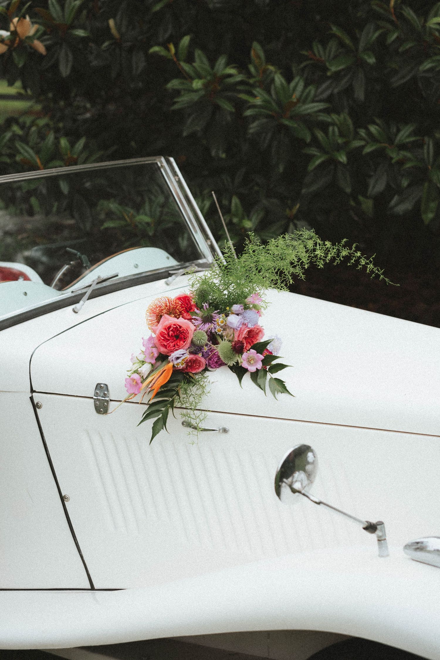 Colorful bridal bouquet with pink roses and greenery displayed on a classic white vintage convertible car.