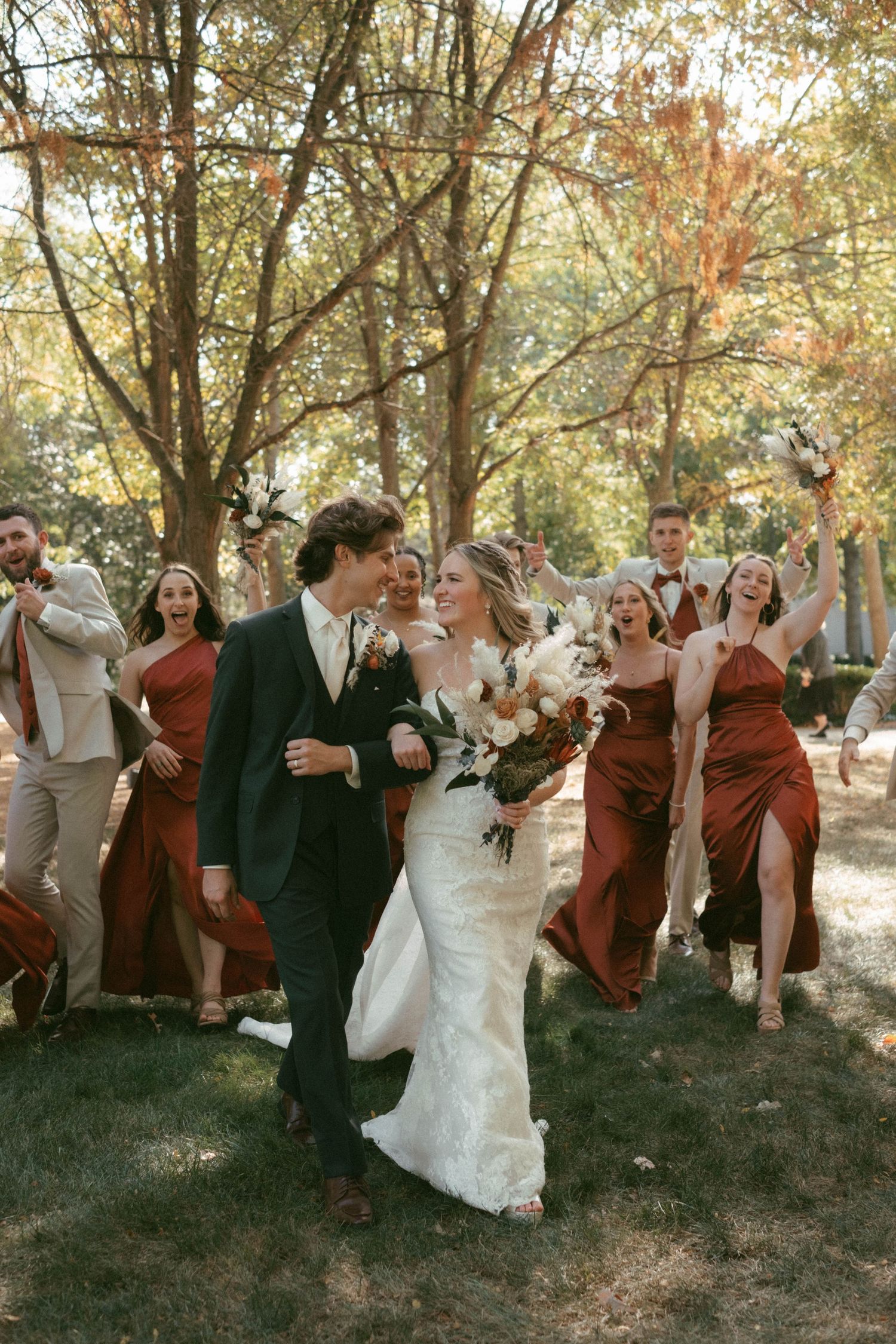 Wedding party members celebrate outdoors wearing burgundy and neutral colored attire.